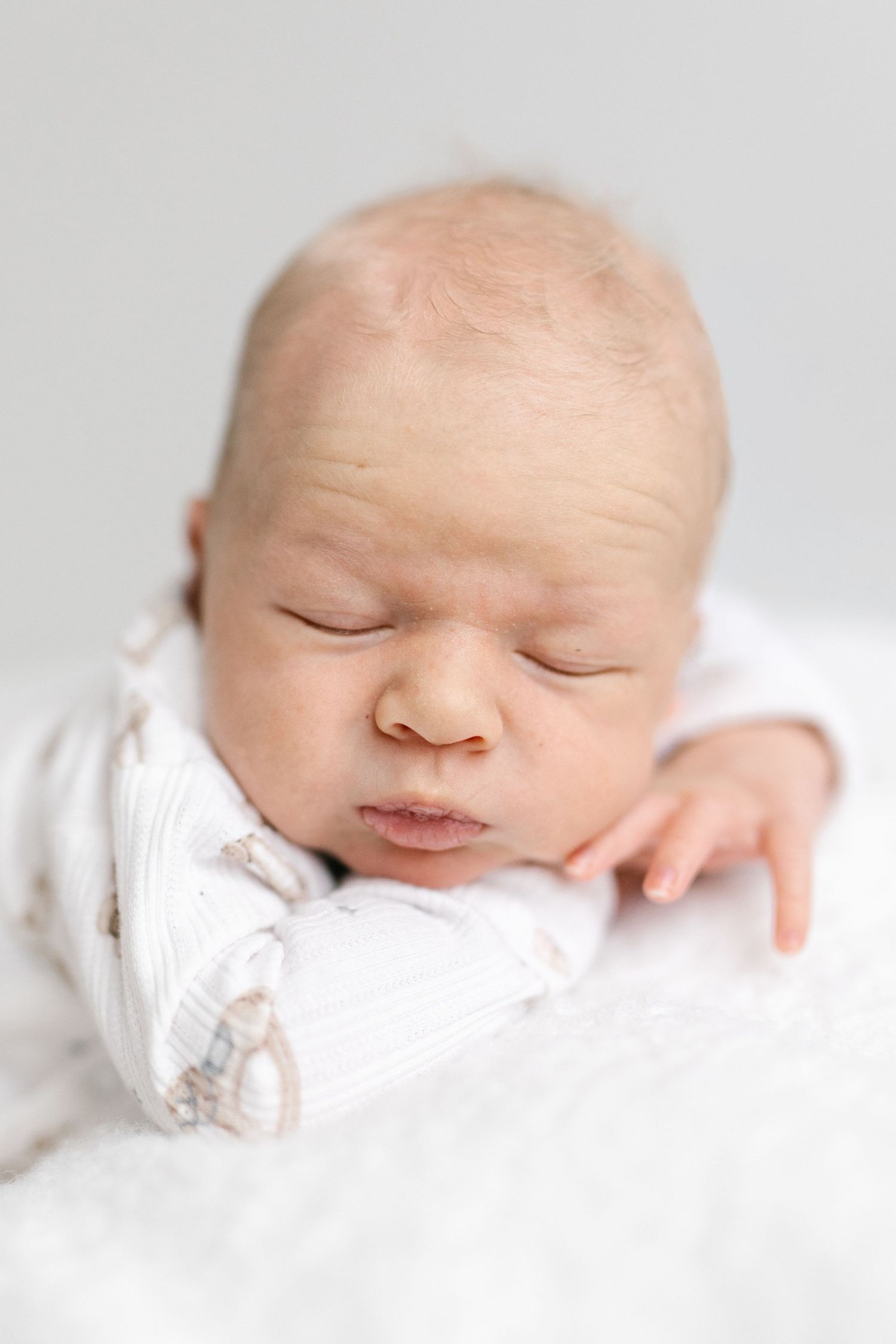 Newborn baby with closed eyes resting on white blanket in soft lighting.