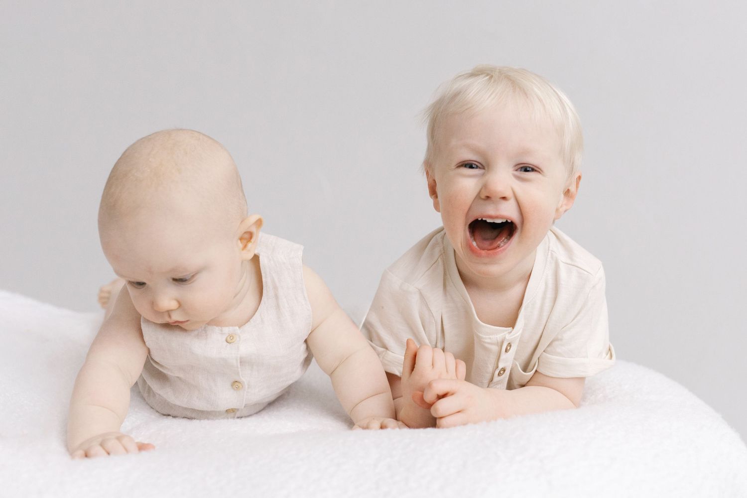 Two young children in light colored outfits playing together on white background.