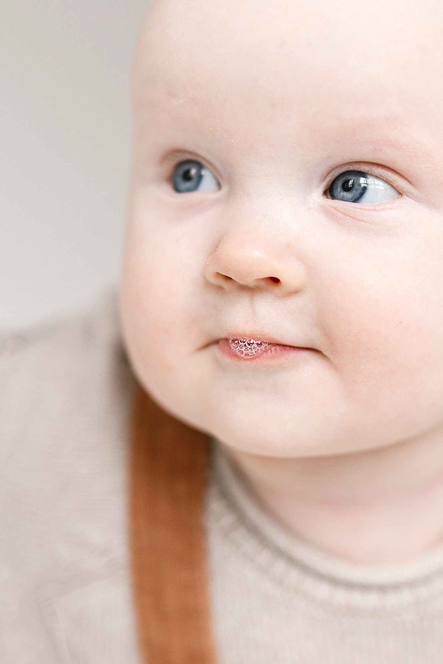 Close-up portrait of an adorable blue-eyed baby with rosy cheeks and a gentle smile, wearing a beige sweater.