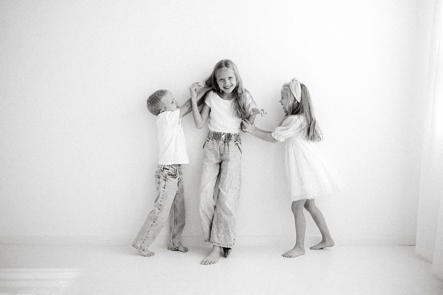 Family members interact playfully on white floor in matching light-colored outfits.