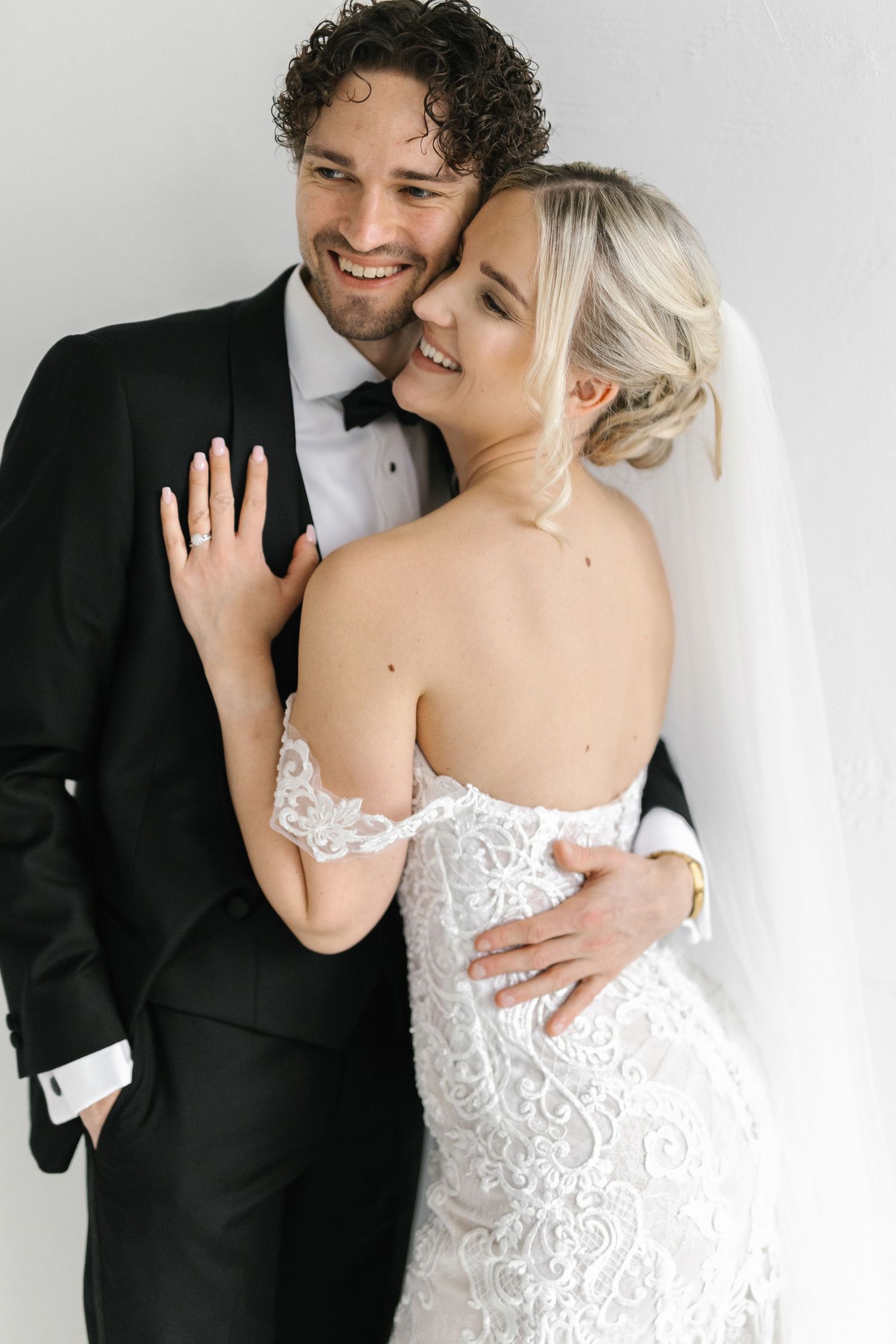 A romantic wedding portrait showing a couple embracing, with the bride in a lace gown and groom in classic tuxedo.