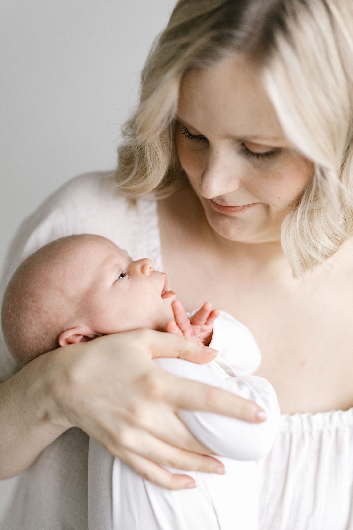 Mother in white dress holding and bonding with newborn baby in tender moments.