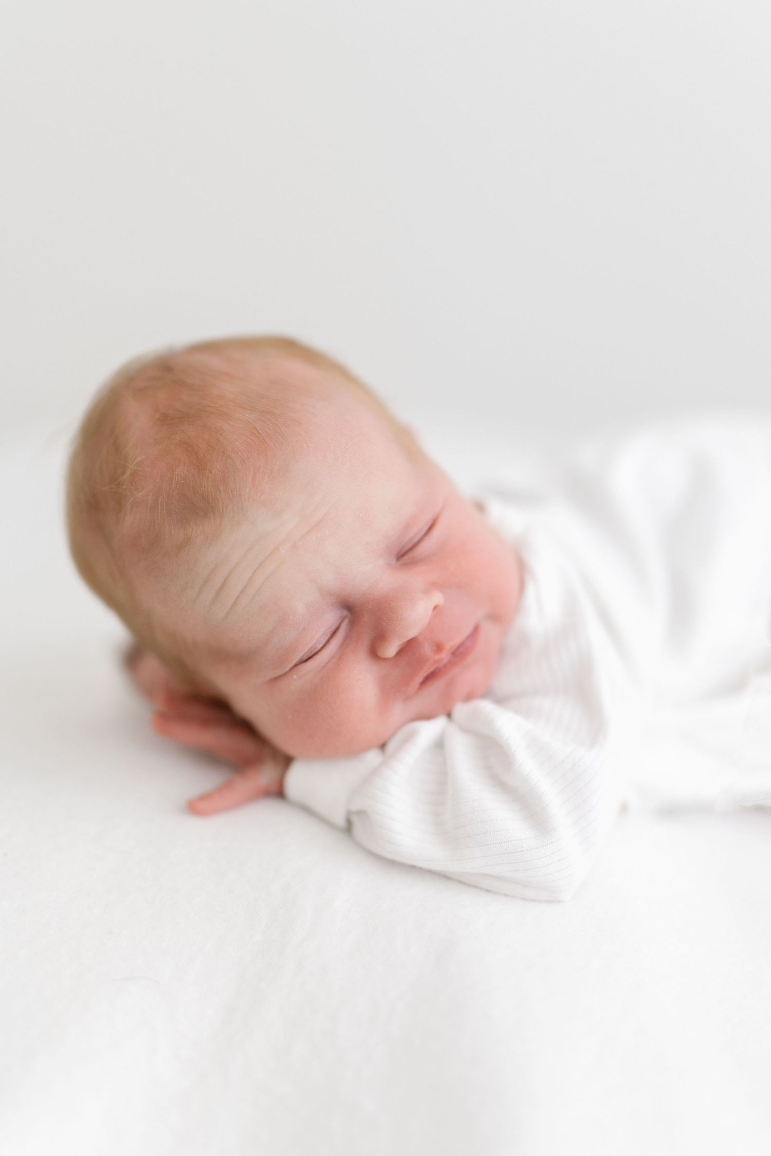 Serene newborn baby sleeping in white outfit on light bedding.