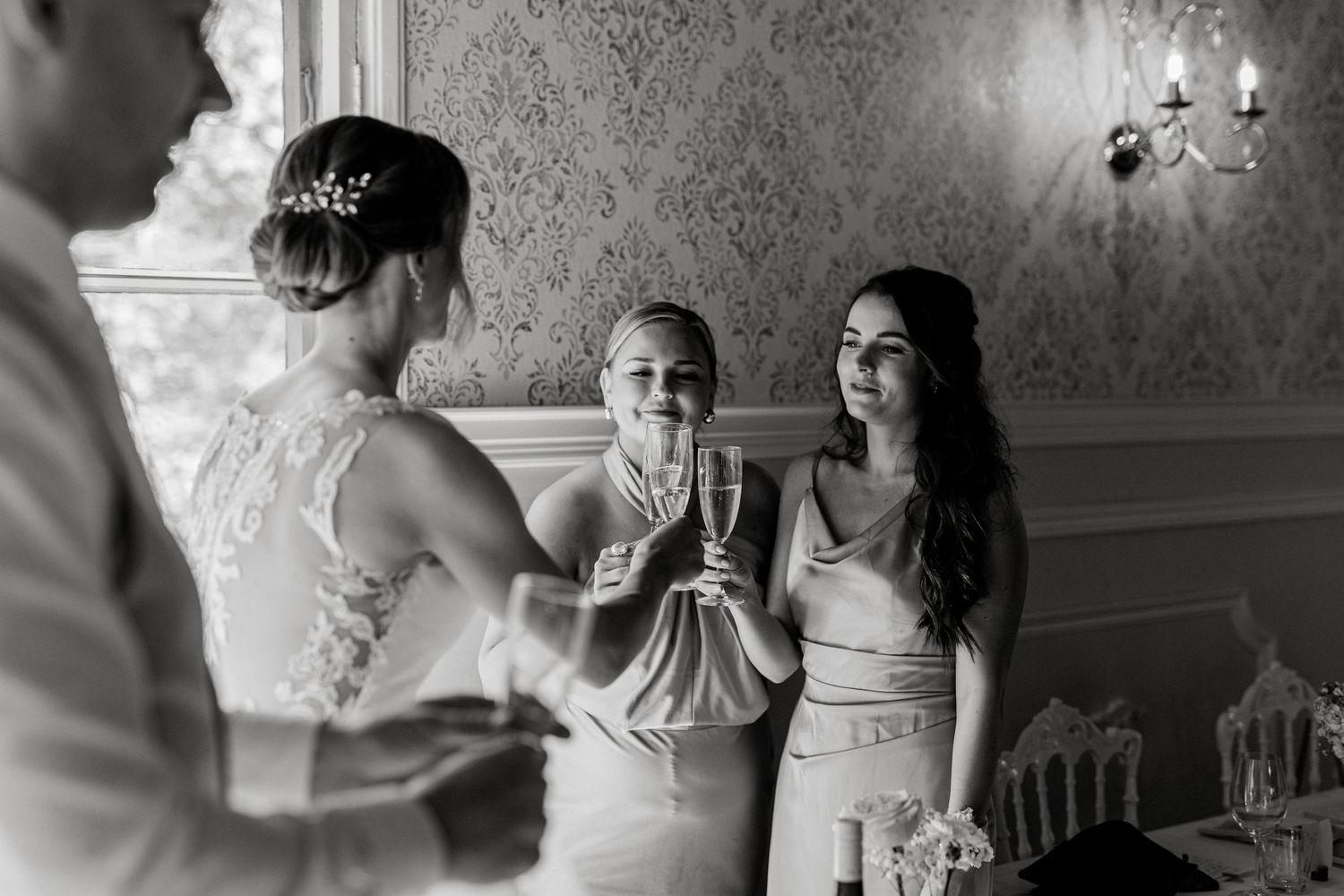 Black and white wedding photo of bride and guests toasting with champagne glasses in elegant venue.