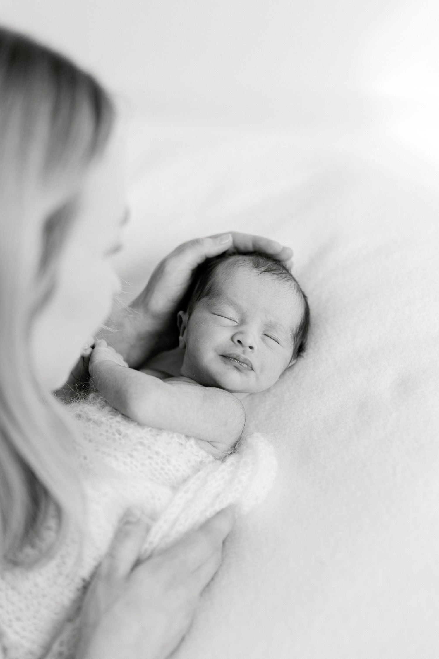 Black and white photo of a newborn baby smiling while being cradled by mother's gentle hands.