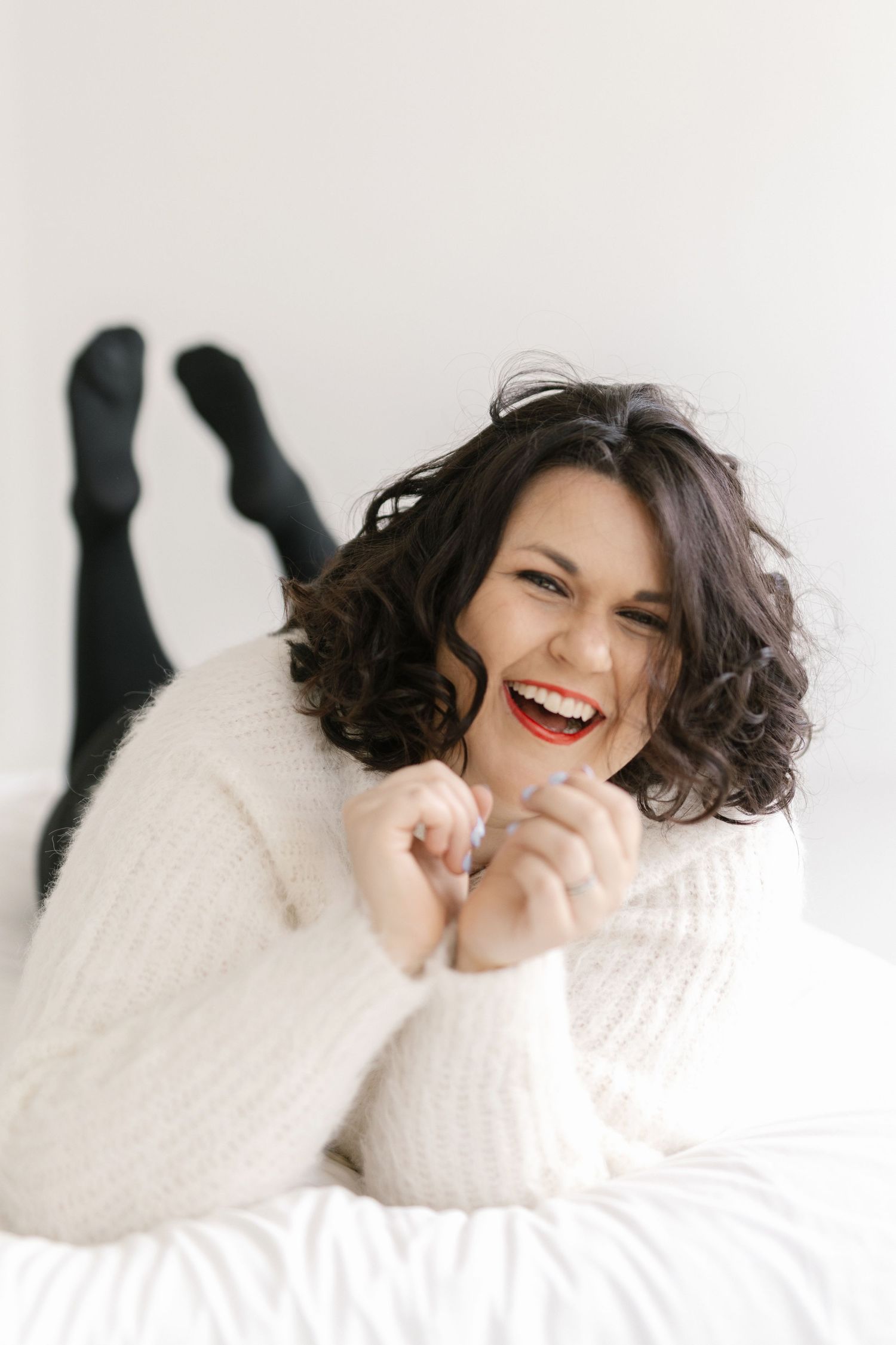 Woman in white sweater laughing joyfully against light background in artistic portrait series.