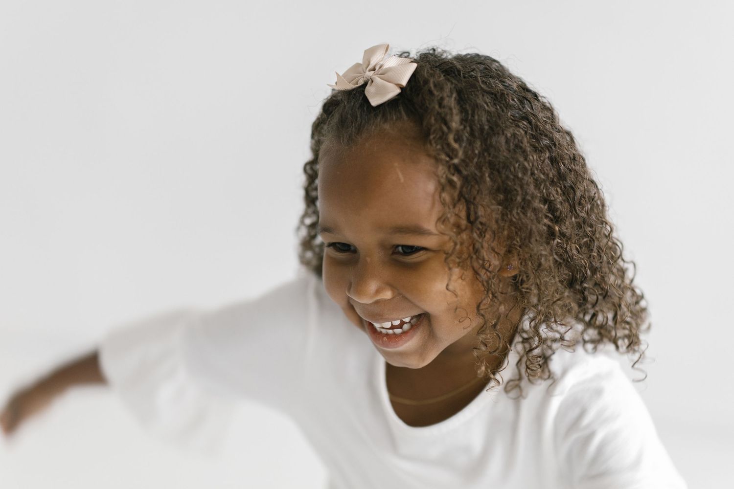 Smiling young Black girl with curly hair and floral hair clip wearing a white t-shirt against a white background.