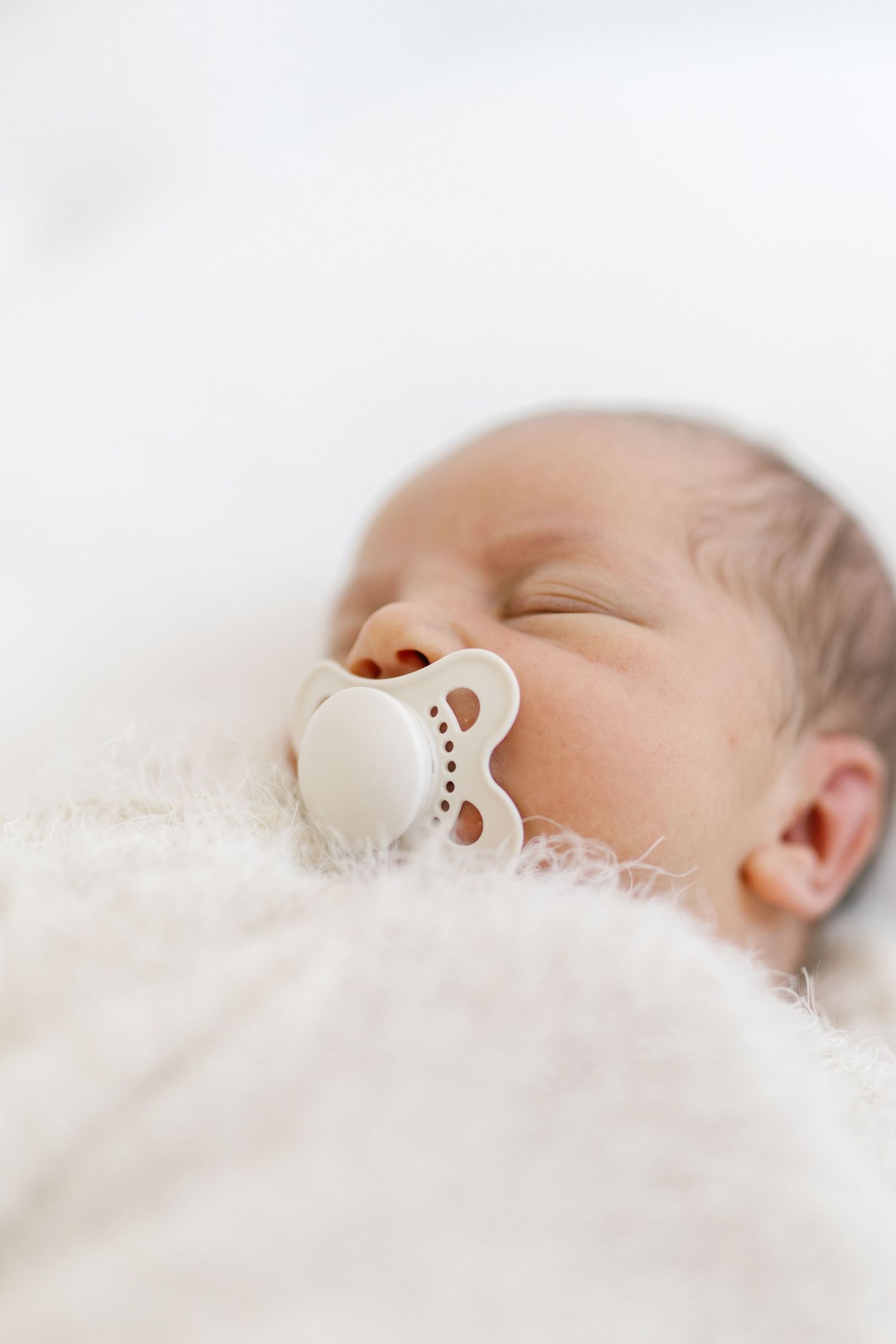 Peaceful newborn baby sleeping with a white pacifier, wrapped in a soft white blanket.