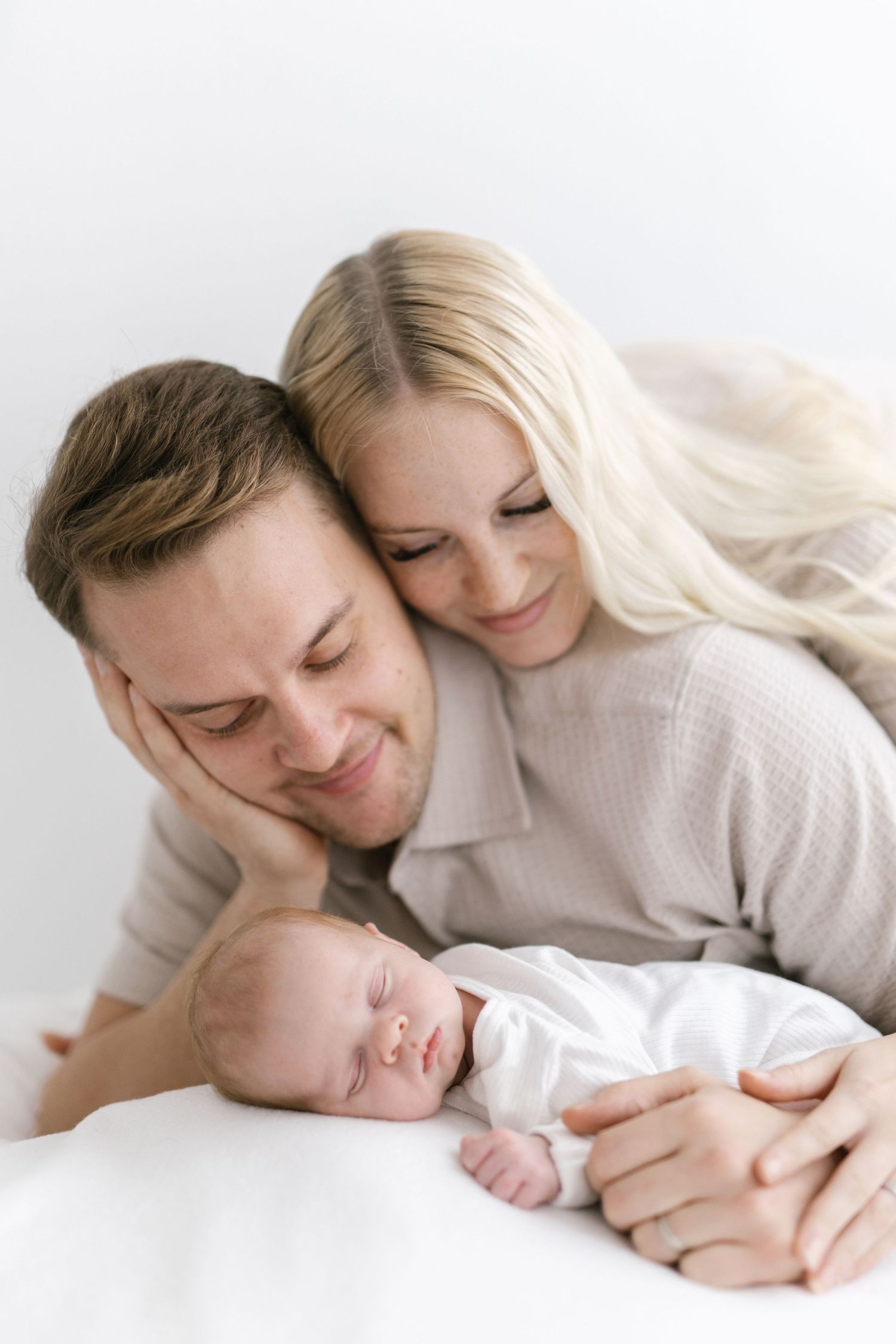 Intimate family portrait with sleeping newborn and parents in soft neutral tones.