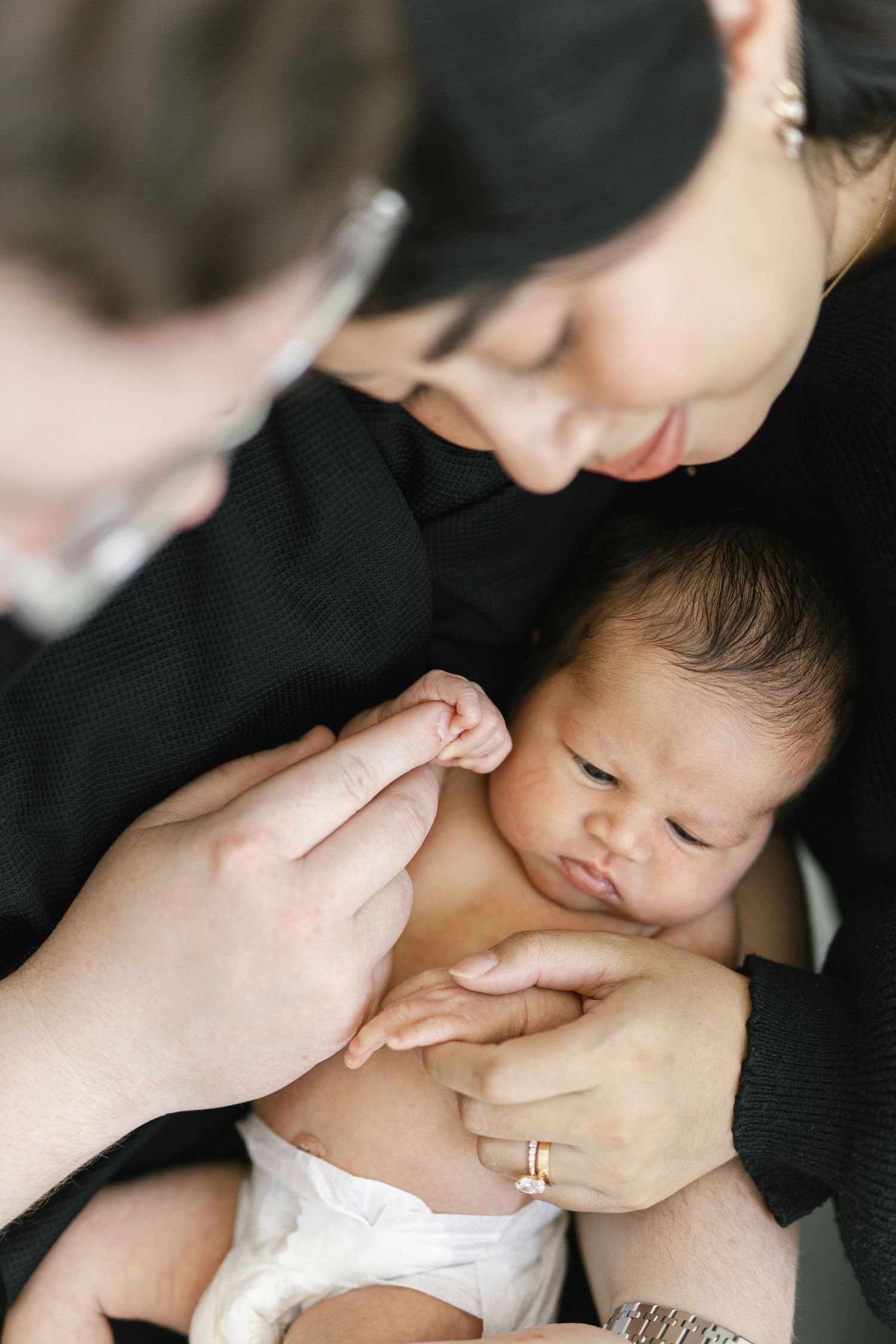 Parents in black outfits tenderly holding their newborn baby, with mother gazing lovingly at the infant.