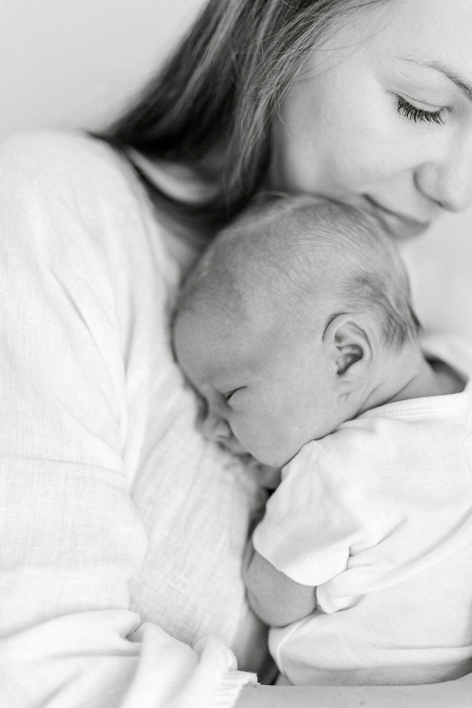 Black and white photo of a mother tenderly cradling and gazing at her sleeping newborn baby.