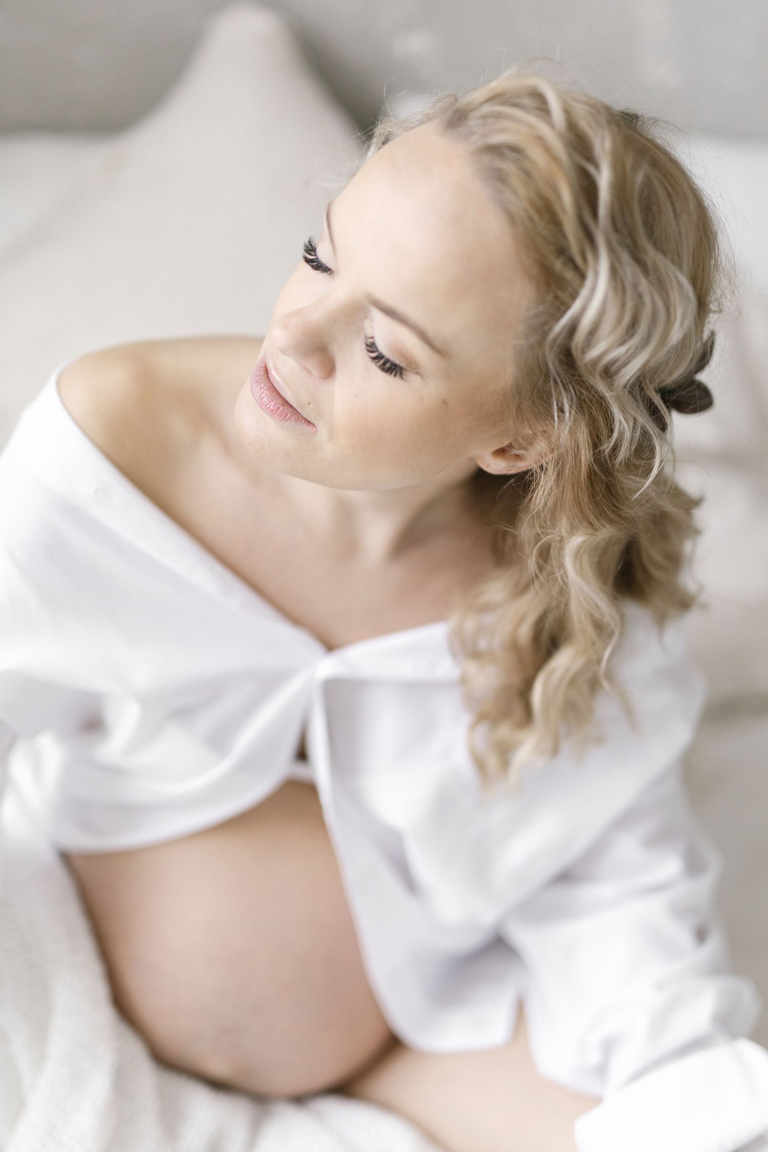 Soft, dreamy maternity boudoir photo with white shirt against light background.