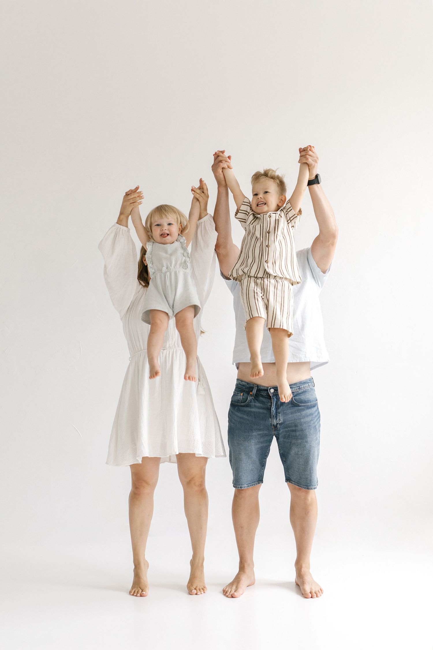 Happy family with two young children lifting kids by hands against white background.