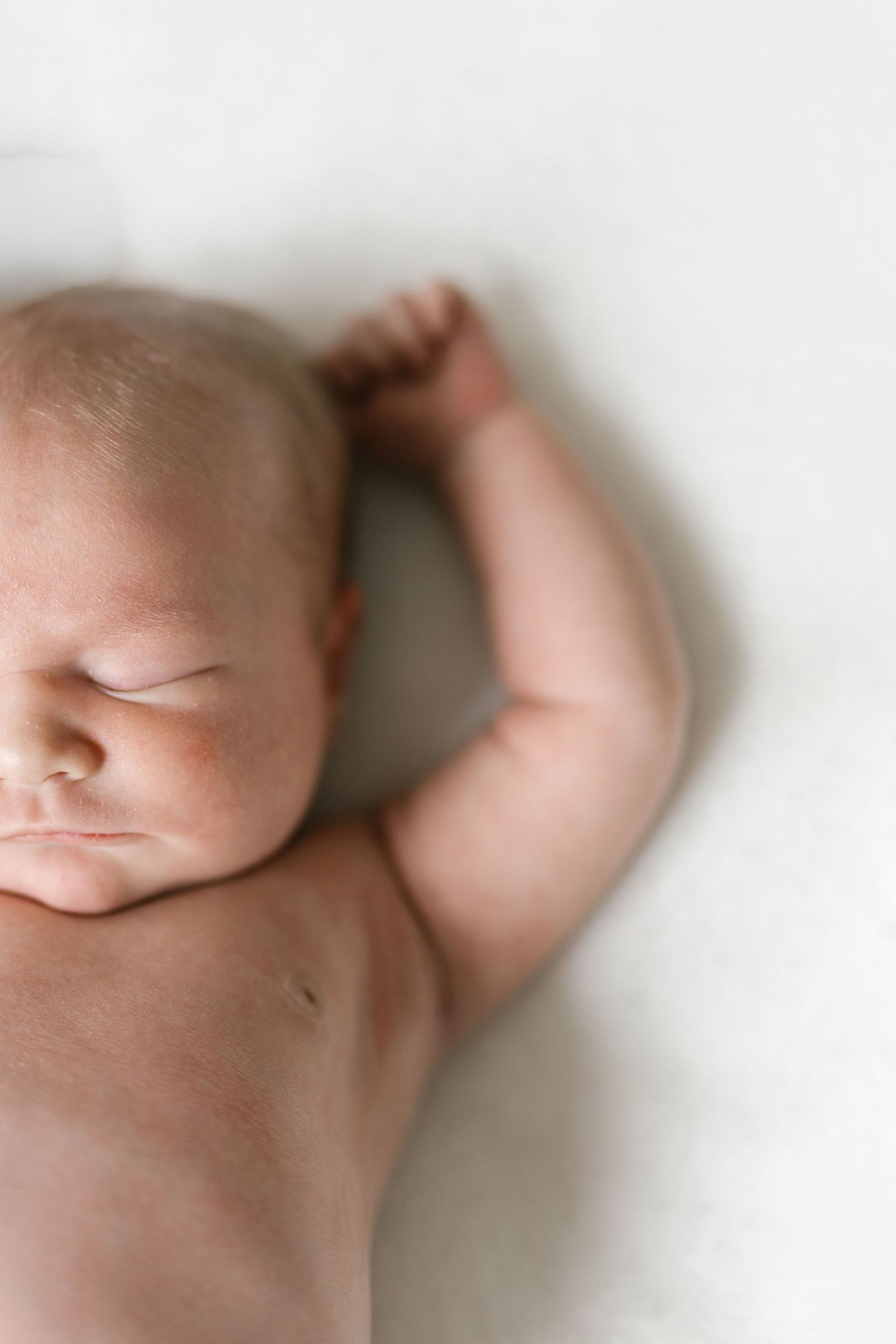 A peaceful newborn baby sleeping on a white blanket, with tiny fist raised and eyes closed.