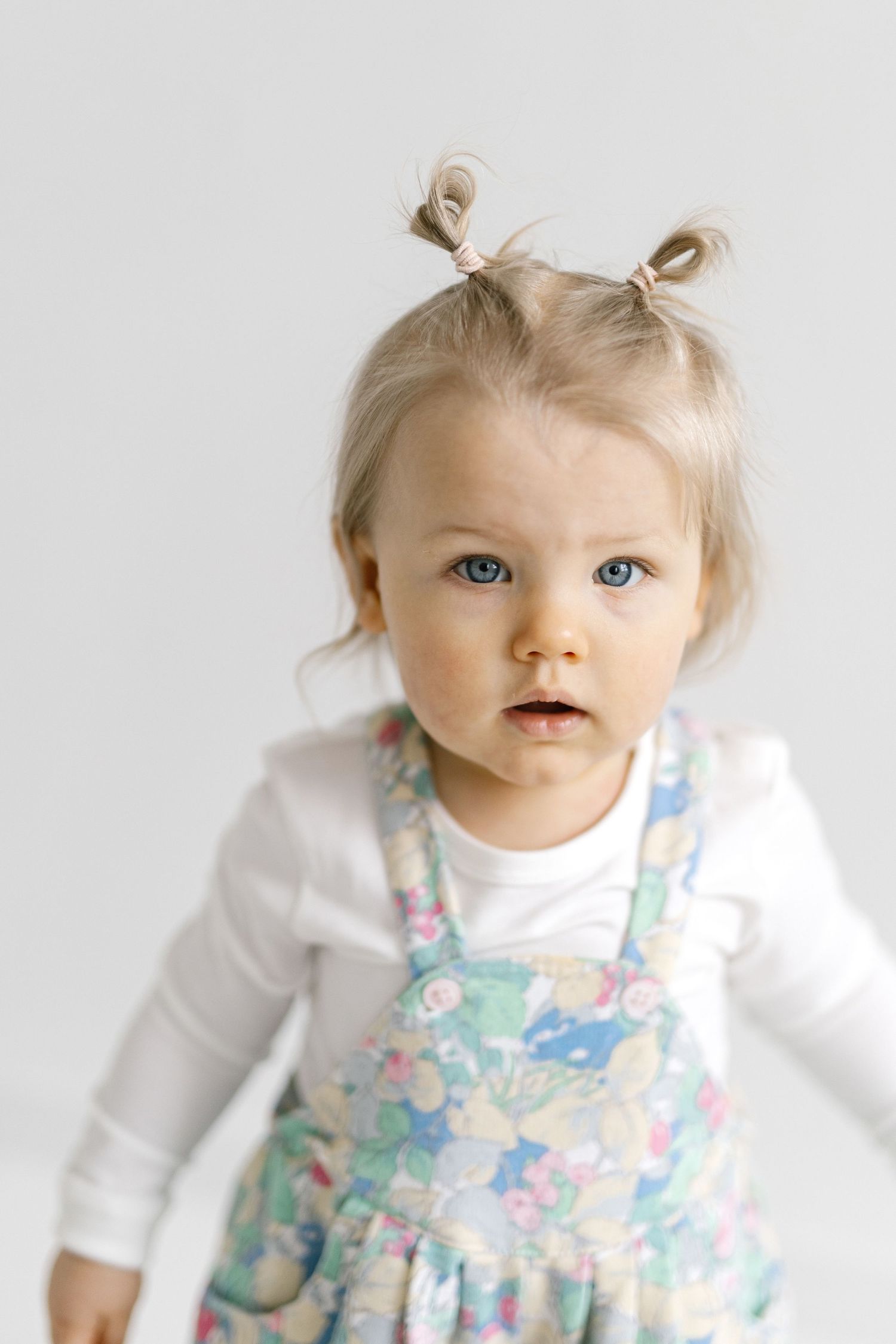 Adorable blonde toddler girl with pigtails and blue eyes wearing a floral dress and white top.