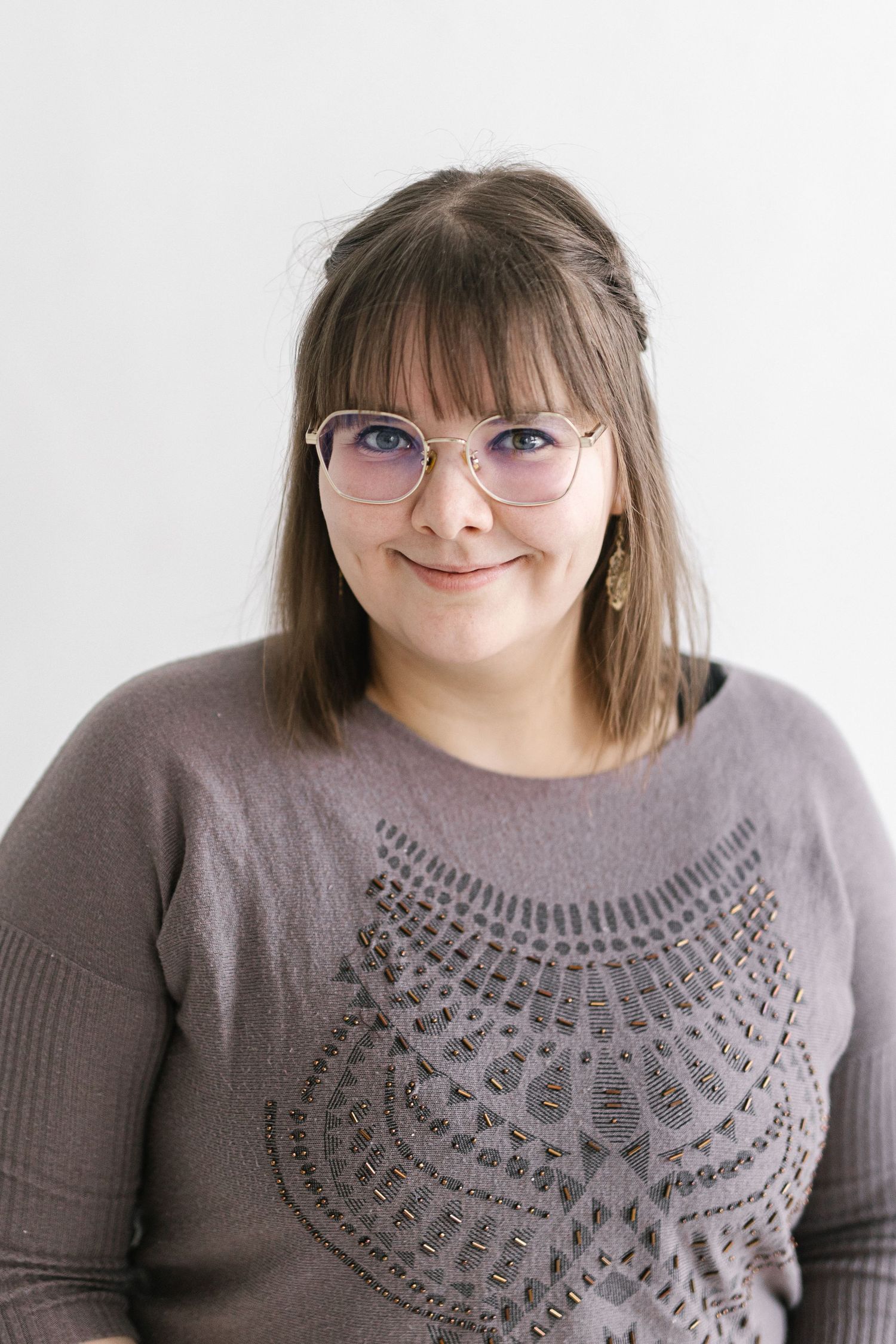 Portrait of someone wearing glasses and a gray sweater with decorative pattern against white background.