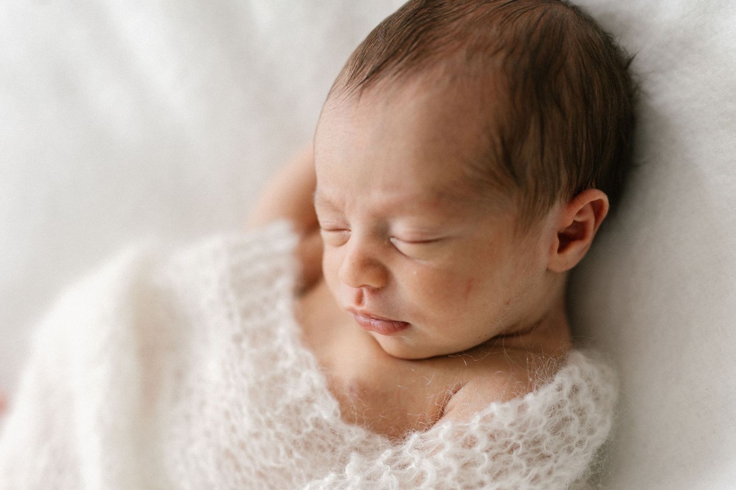 Peaceful newborn baby sleeping wrapped in a soft white knit blanket, eyes closed in serene slumber.