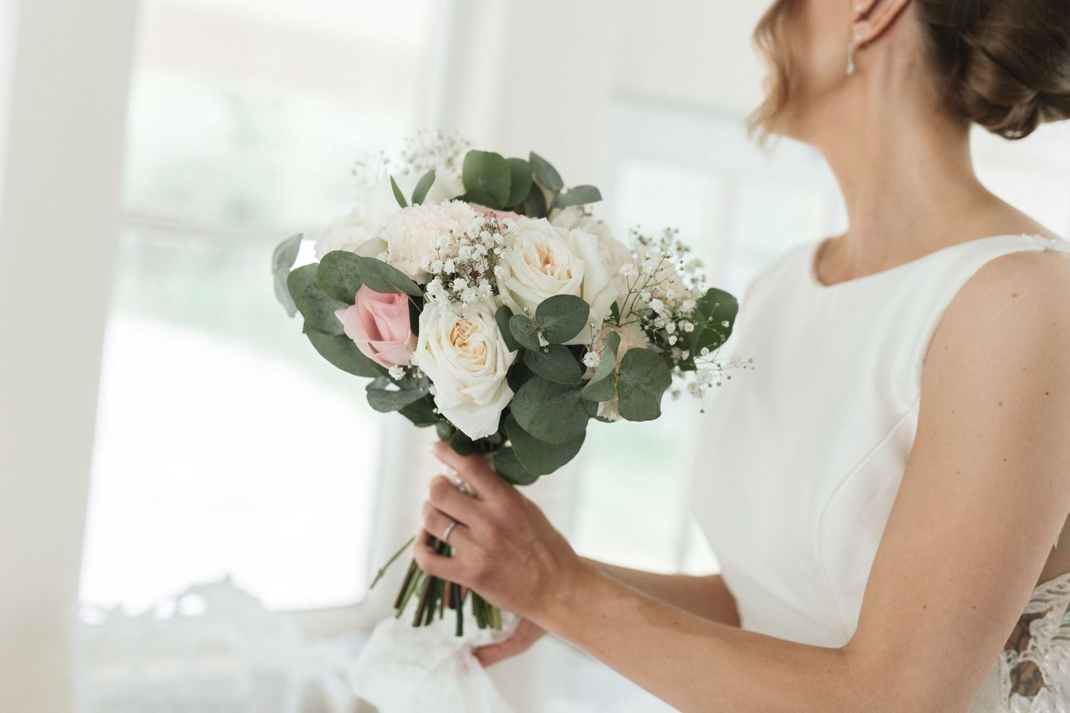 Bride in white dress holding elegant wedding bouquet with pink roses, white blooms, and eucalyptus greenery.