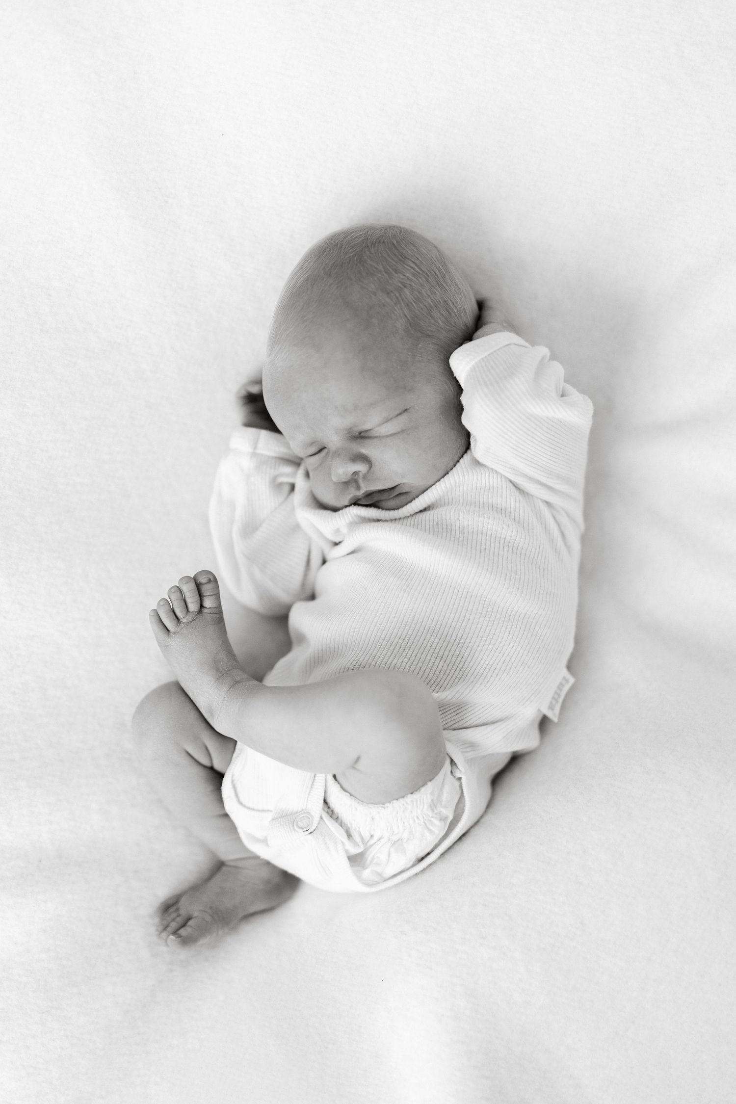 Black and white photo of a peaceful newborn baby sleeping curled up on a soft white blanket.