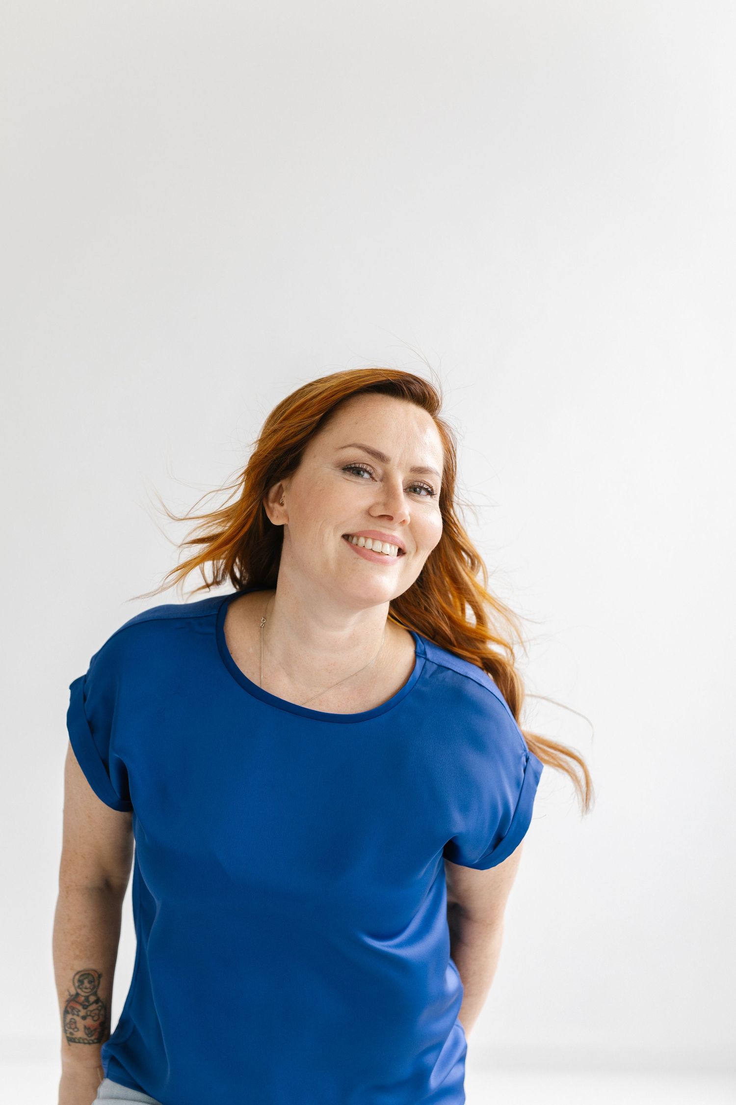 Person in bright blue t-shirt with red hair smiling against white background.