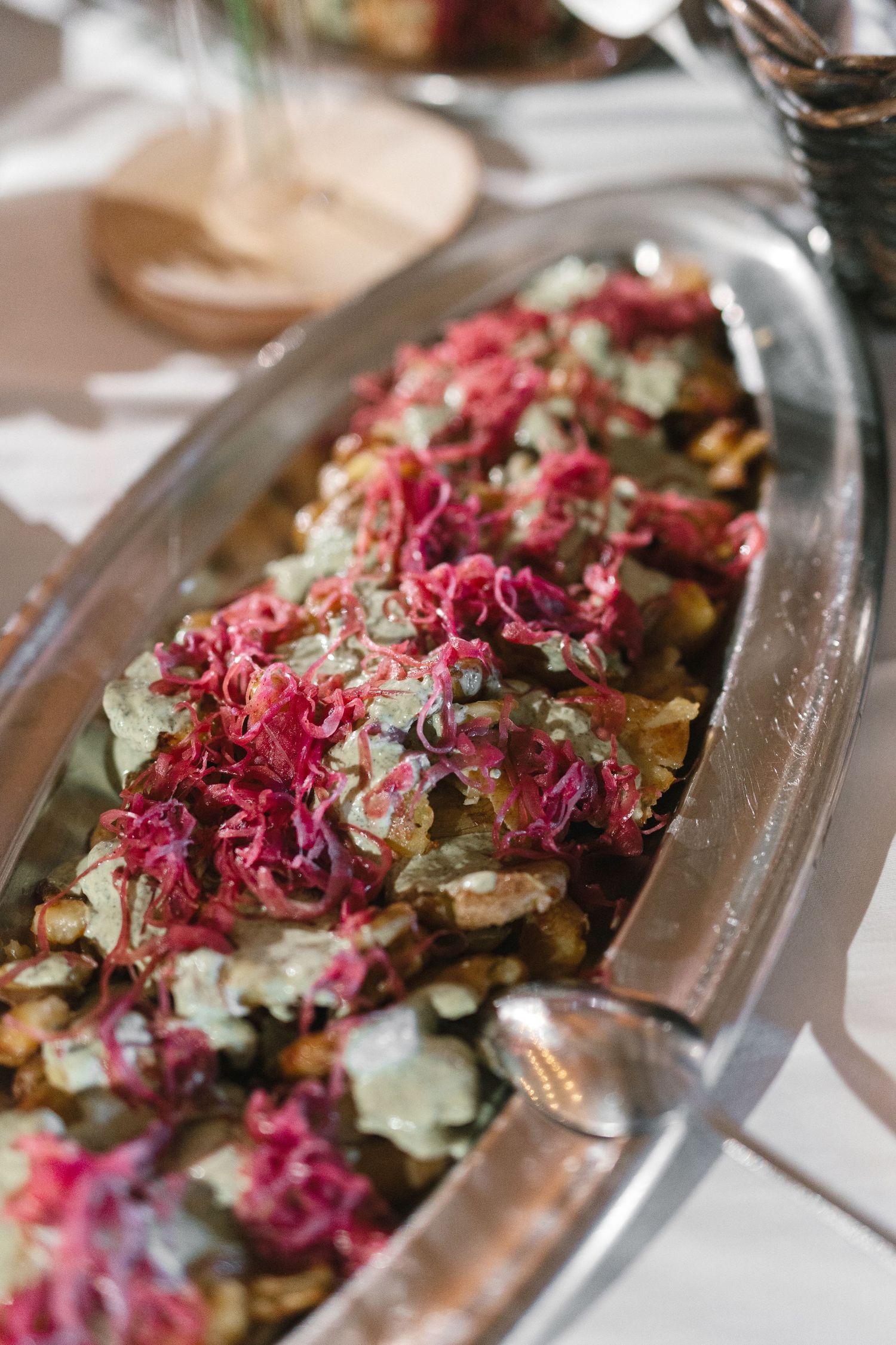 Elegant oval glass dish with roasted vegetables topped with vibrant pickled red cabbage, served on a white tablecloth.