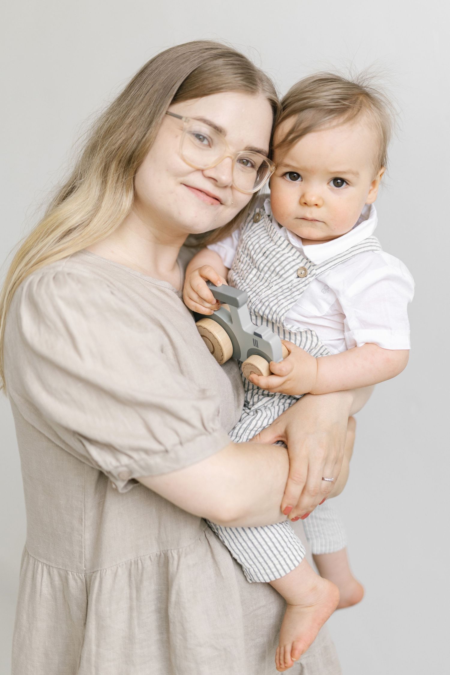 Baby in striped outfit being held against light background.