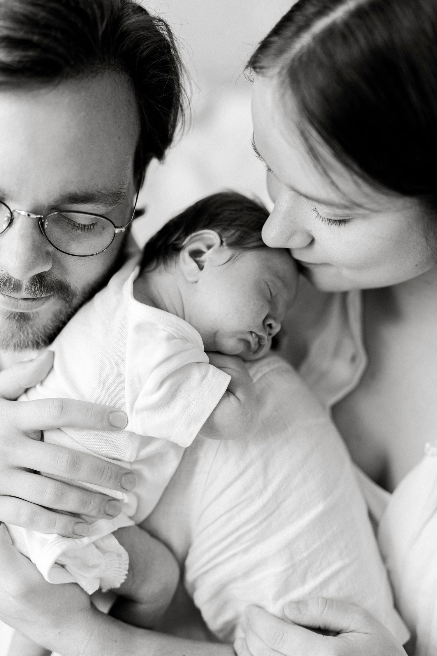 Black and white photo of parents lovingly holding their sleeping newborn baby close.