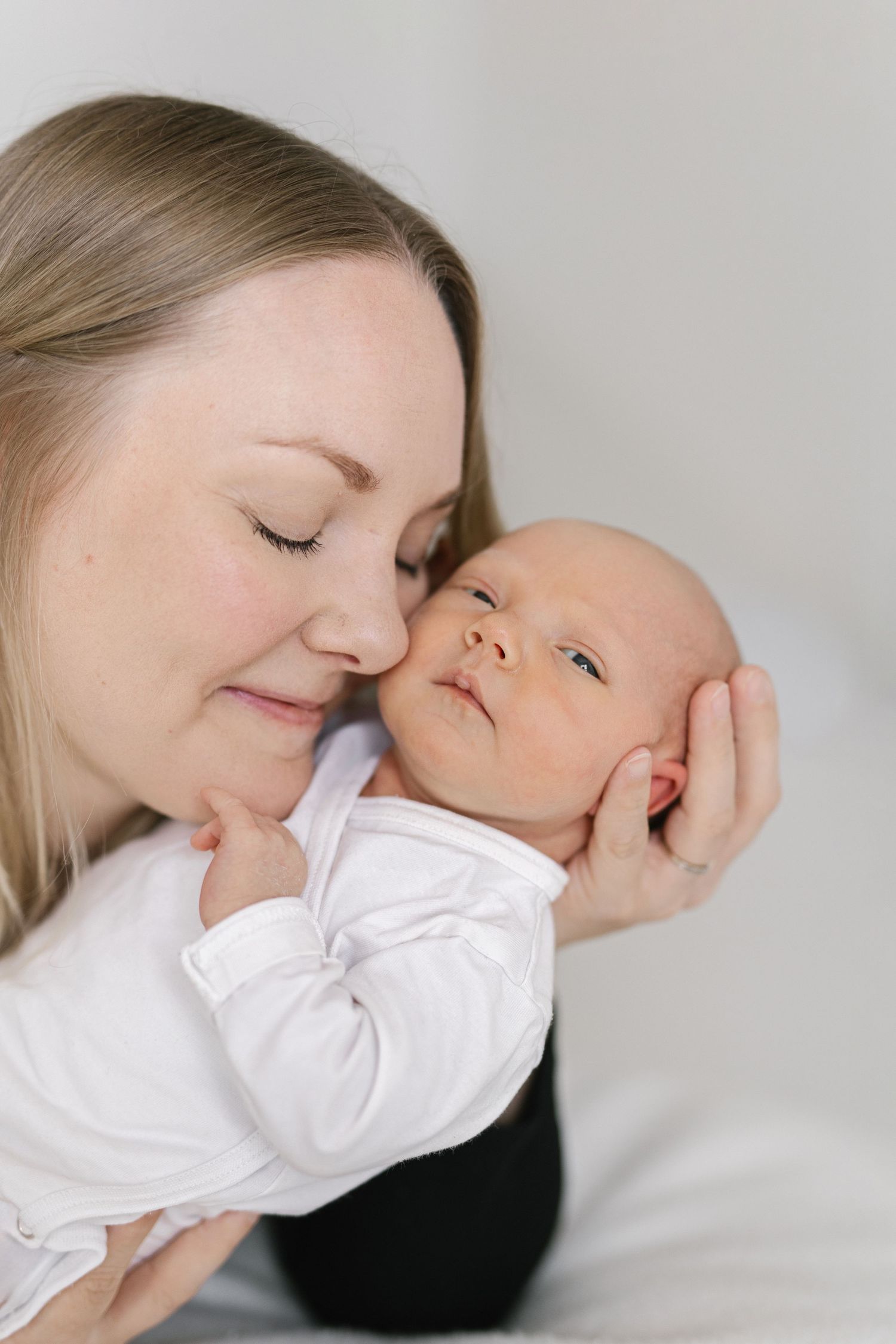 A mother tenderly nuzzles her newborn baby, both dressed in white, sharing a peaceful intimate moment.