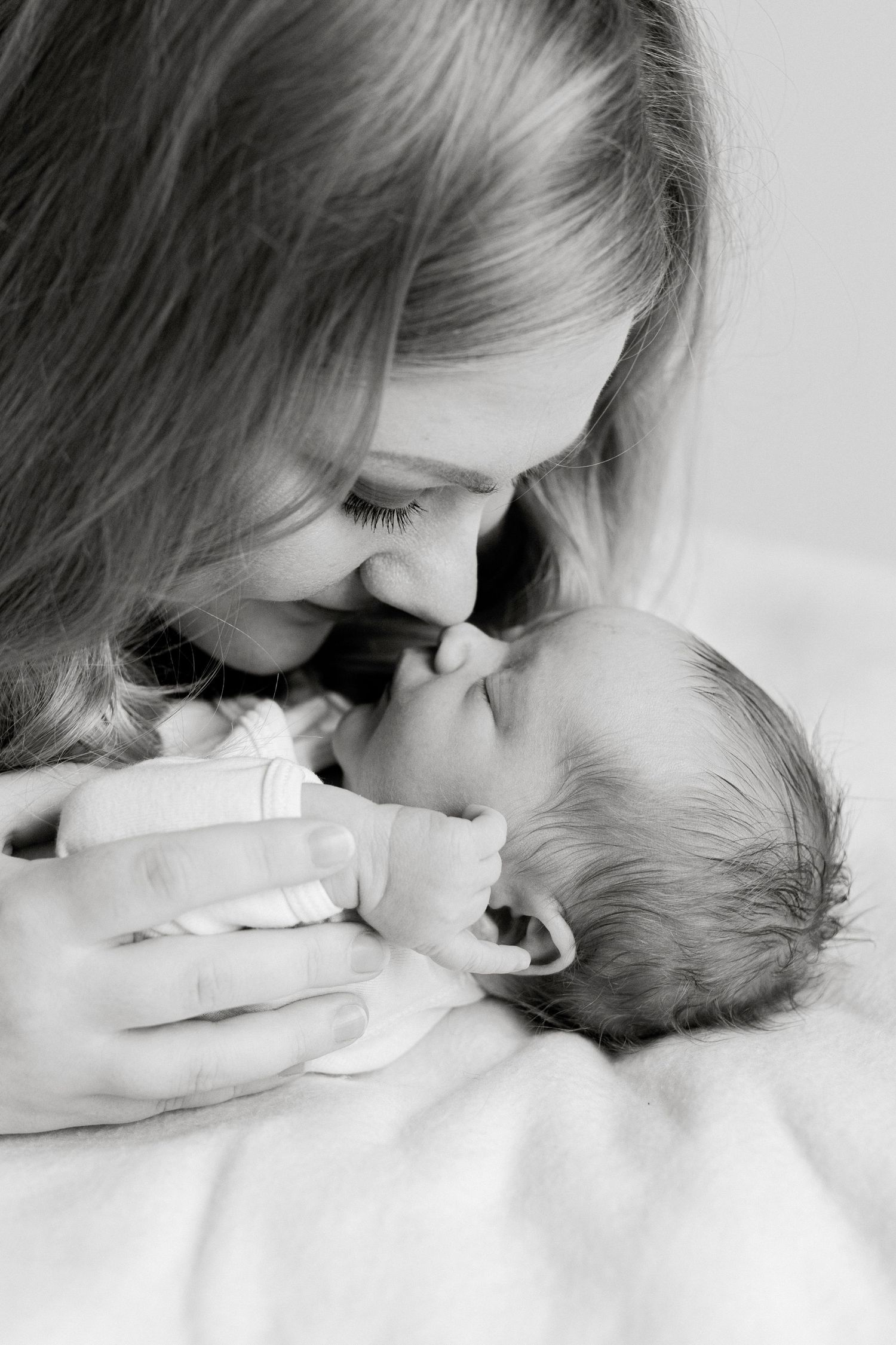 Intimate black and white moment between mother and newborn sharing a tender embrace.