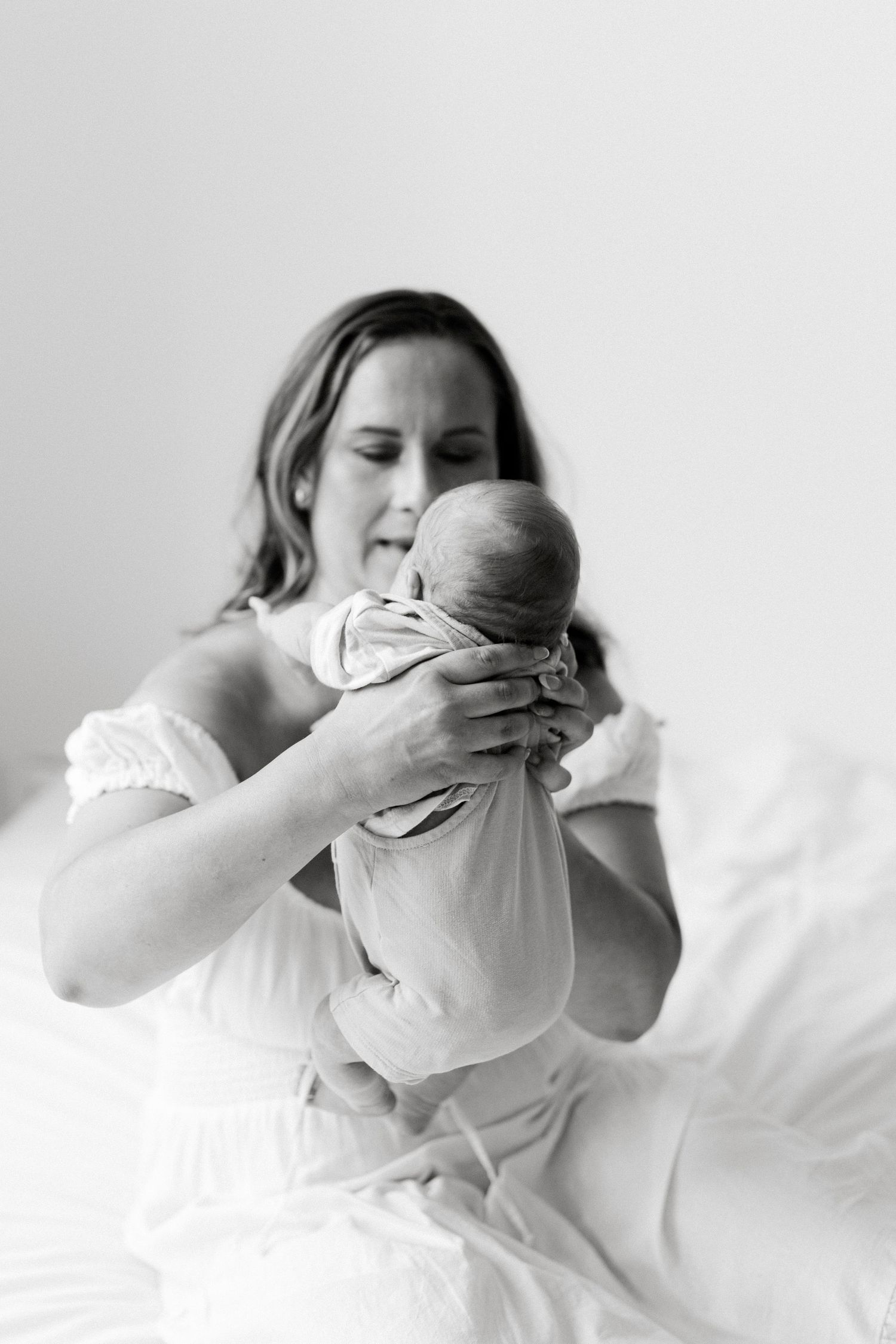 High-key portrait of parent holding sleeping newborn baby against white background.