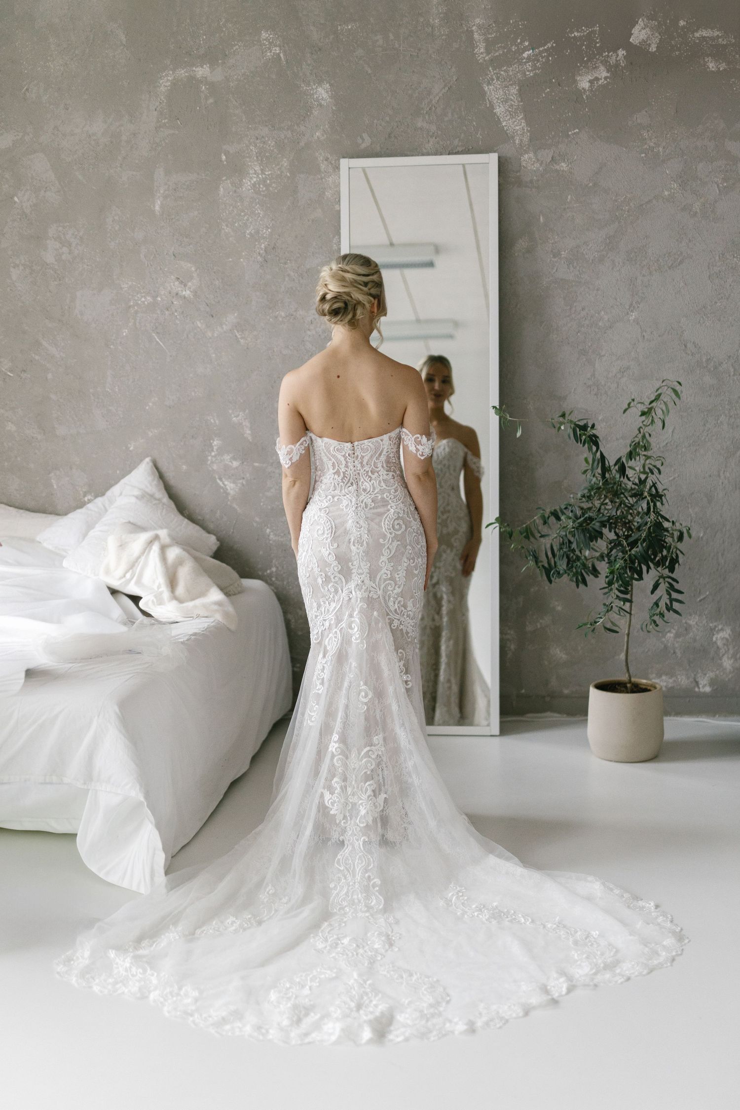Elegant lace wedding dress with flowing train displayed against minimalist grey backdrop.