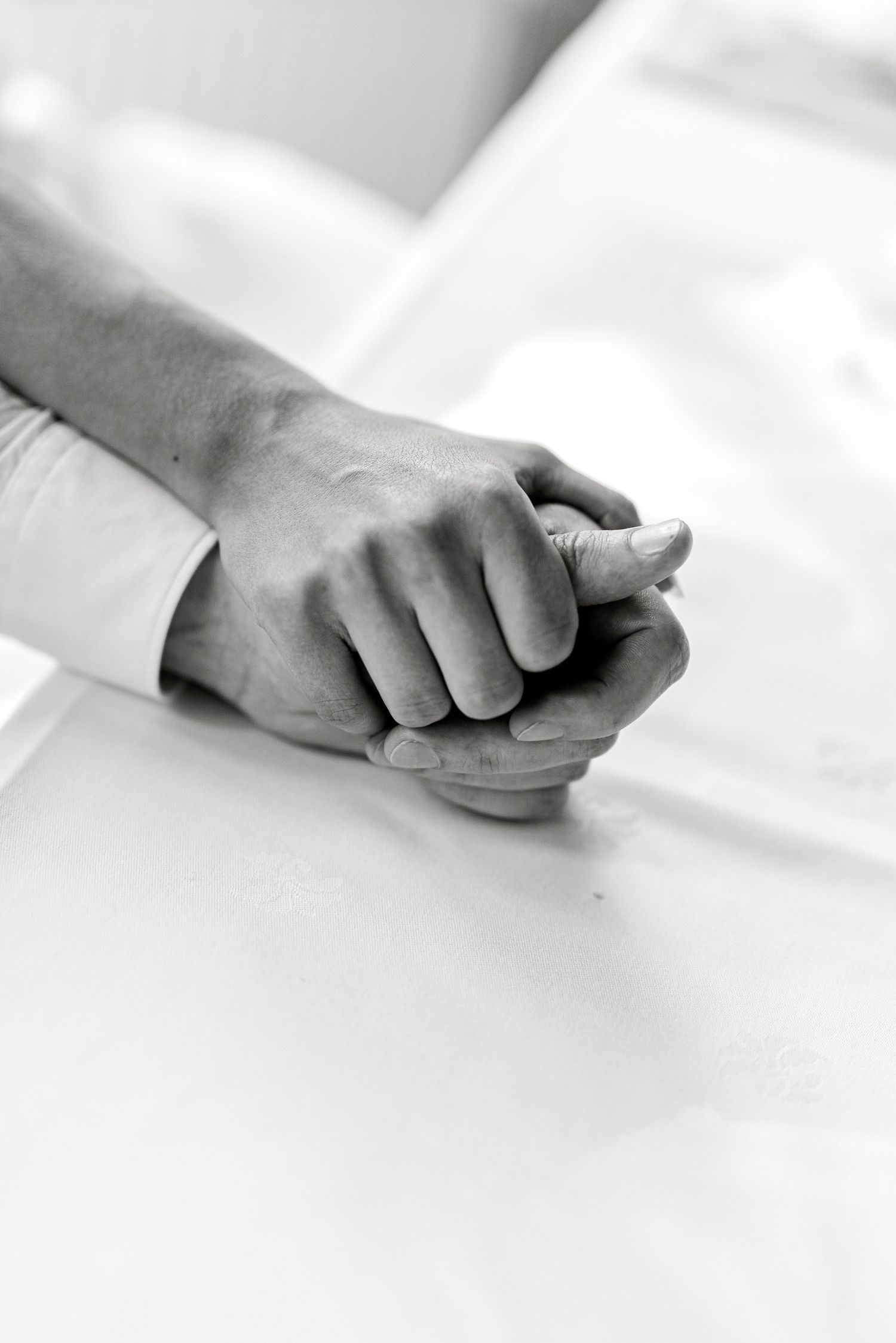 Black and white photo of two people holding hands tenderly, symbolizing comfort and support.