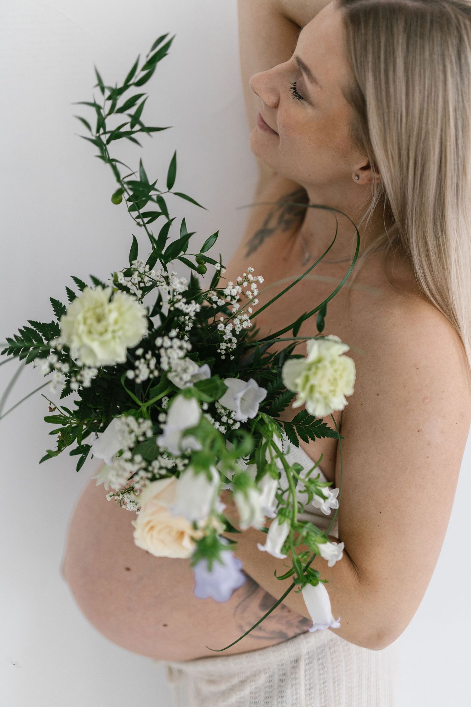 Close-up of pregnant woman holding elegant white roses and greenery bouquet.