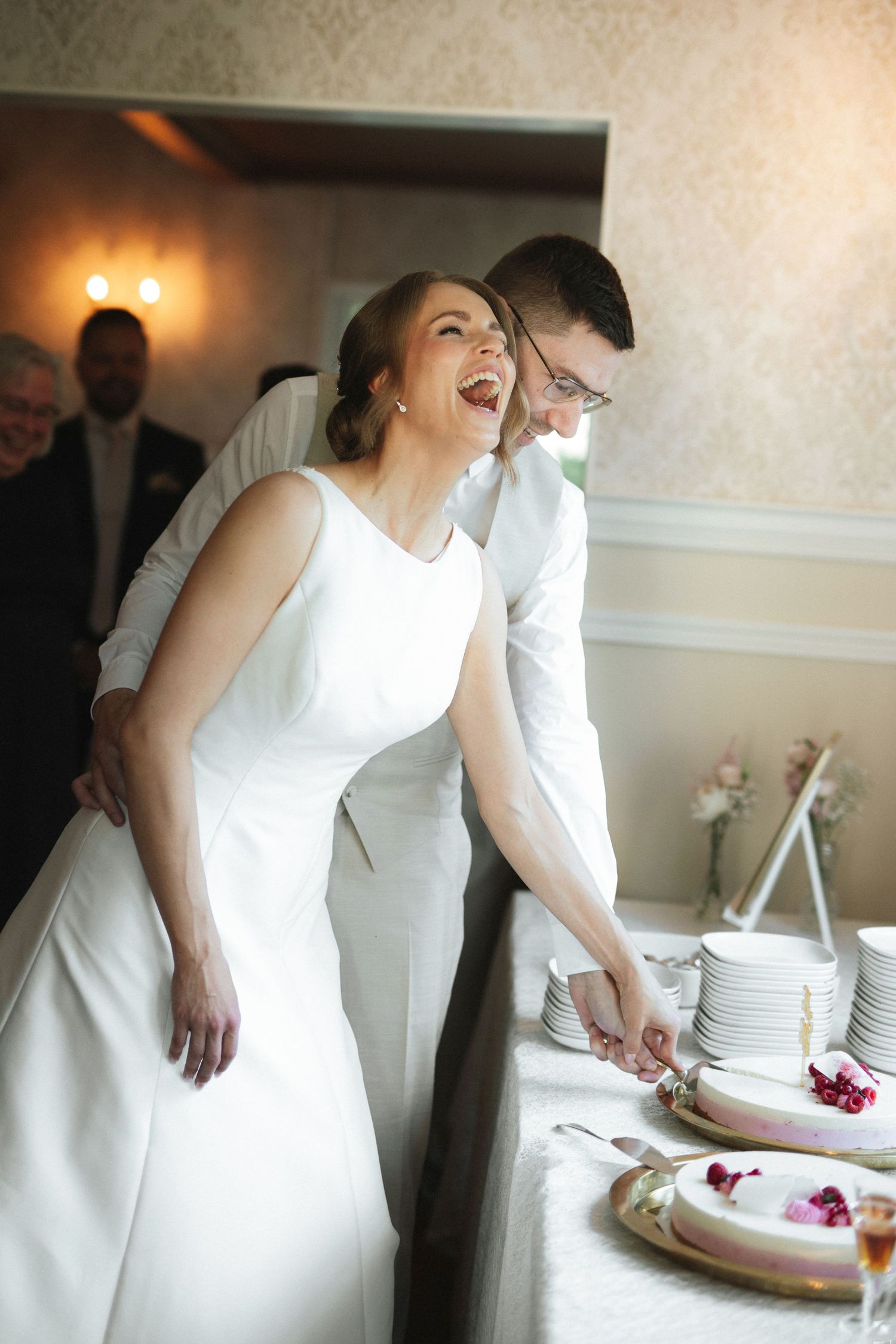 Bride and groom laughing joyfully while cutting their wedding cake together at elegant reception venue.