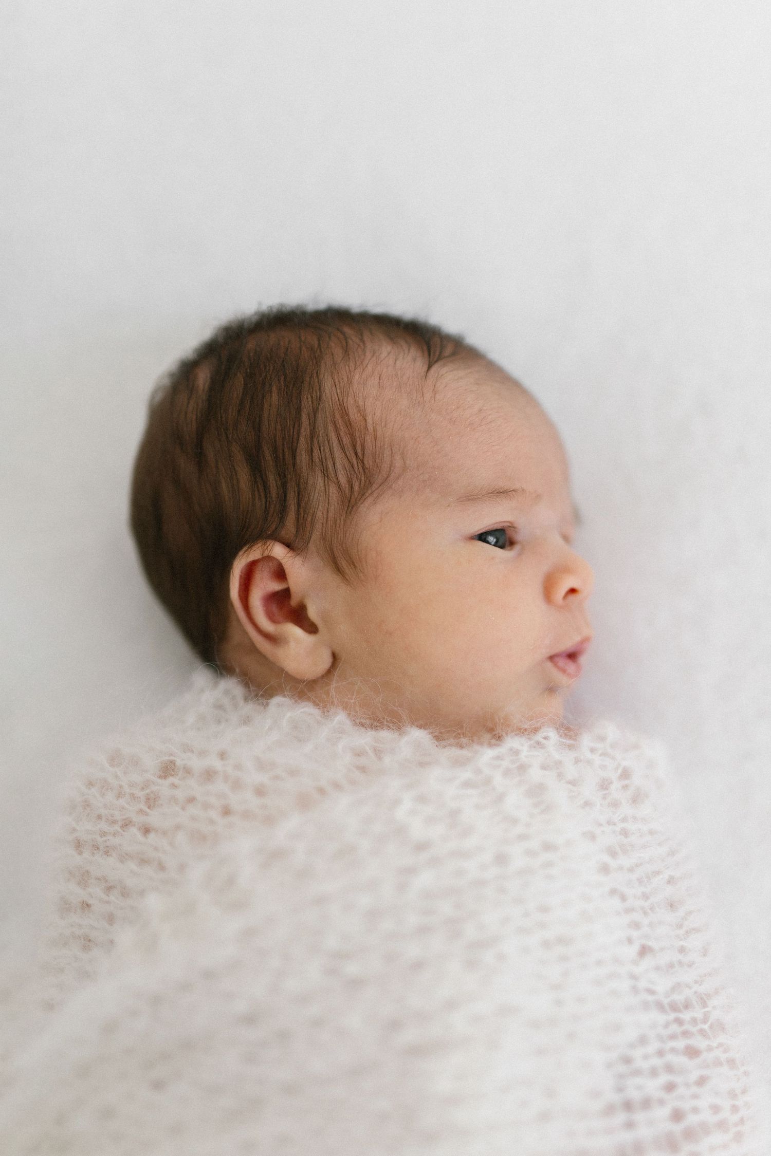 A newborn baby wrapped in soft white lace fabric photographed from different angles in profile view against a light background.