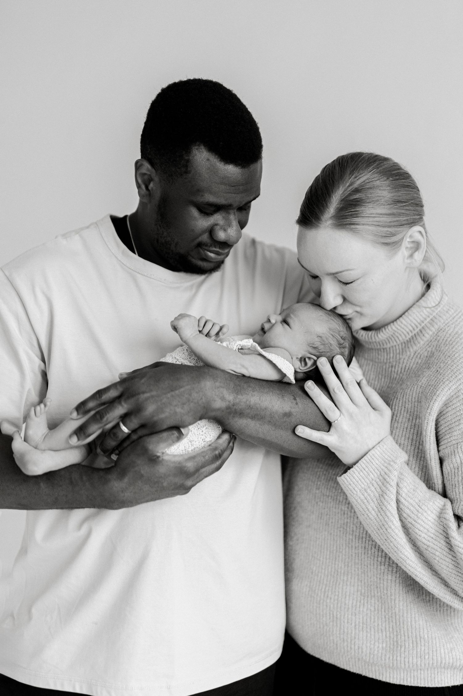 Black and white portrait of parents gazing lovingly at their newborn baby.