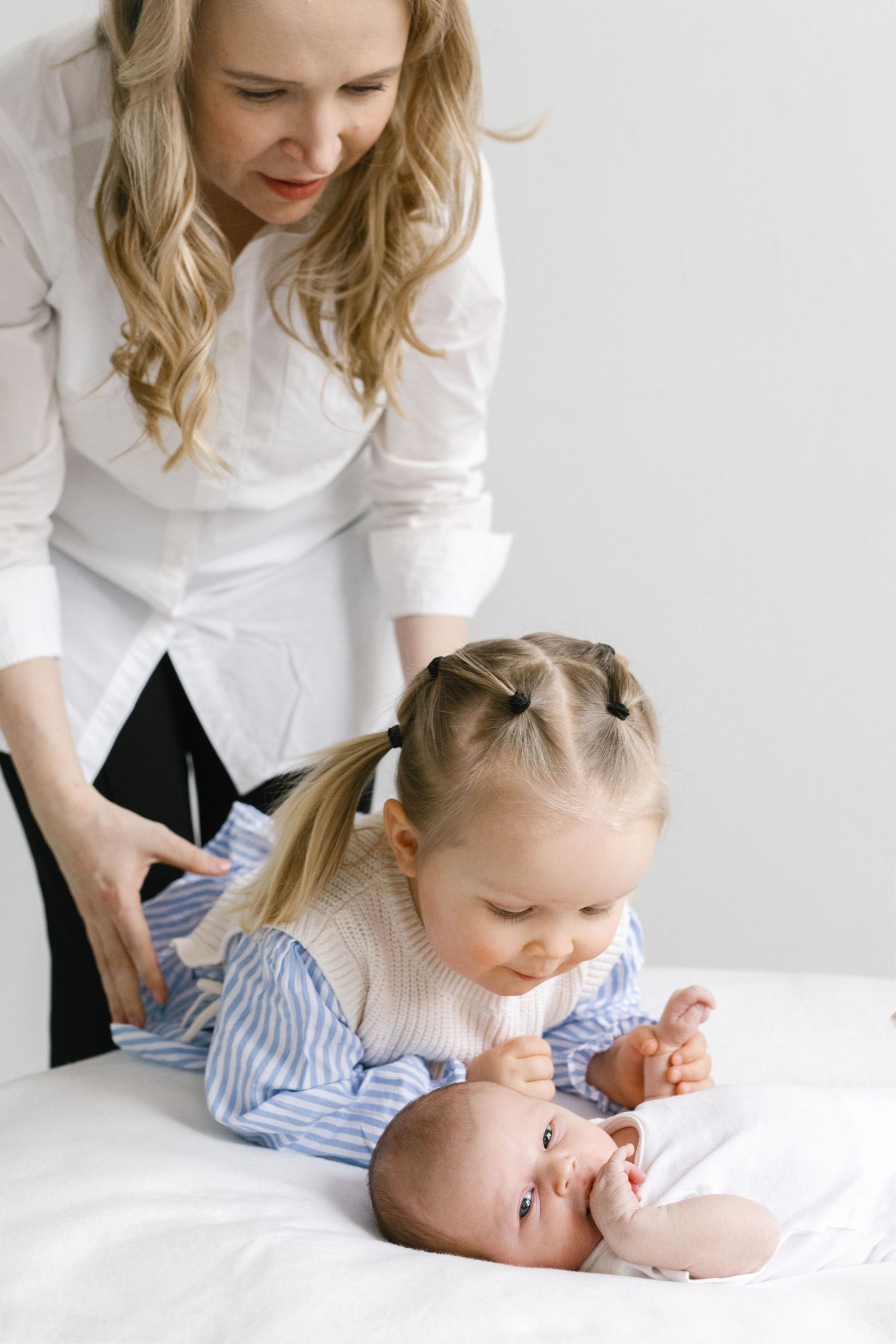 Family members in white clothing gather around to interact with a baby on white bedding.