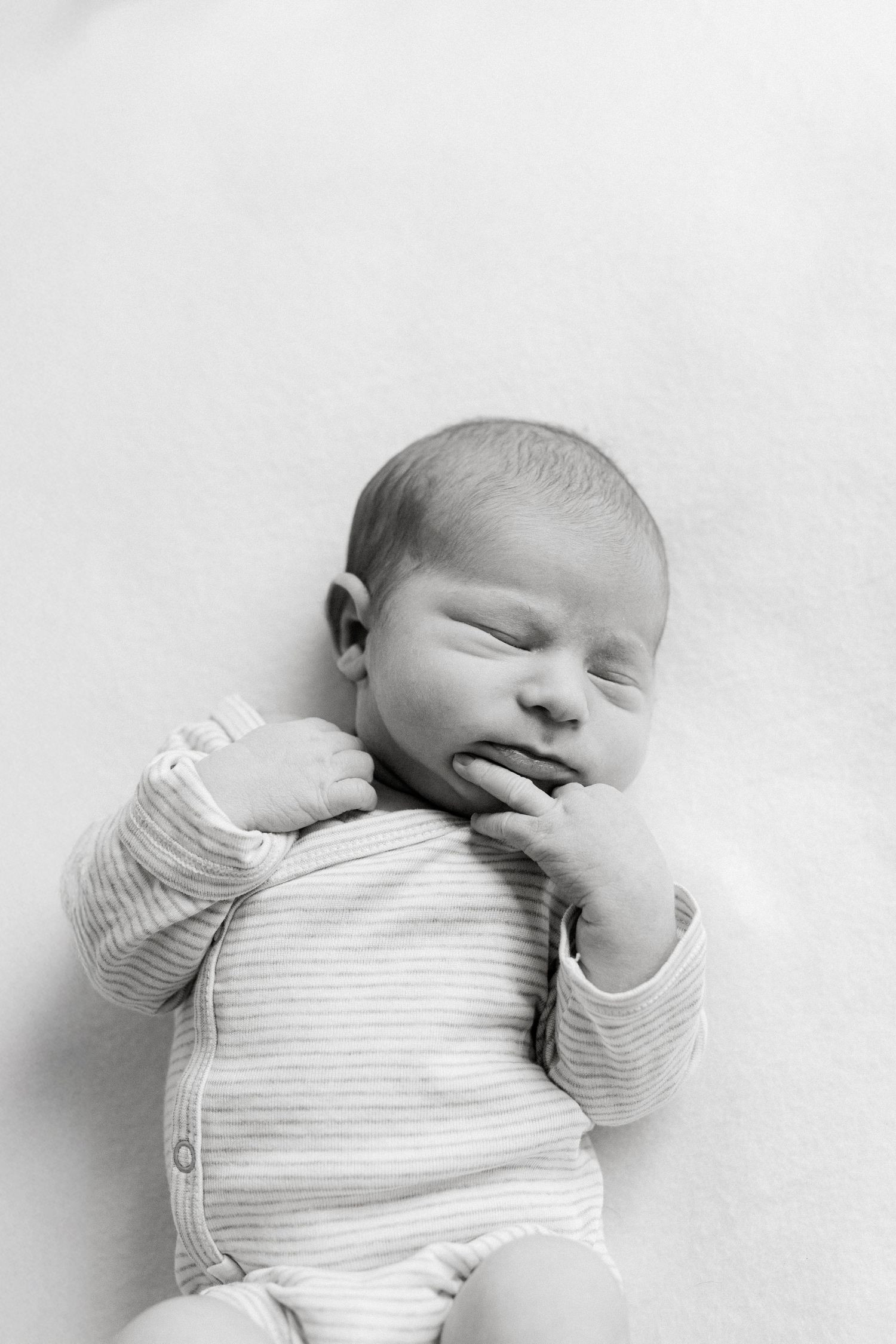 Black and white series of a sleeping newborn baby wearing a striped onesie.