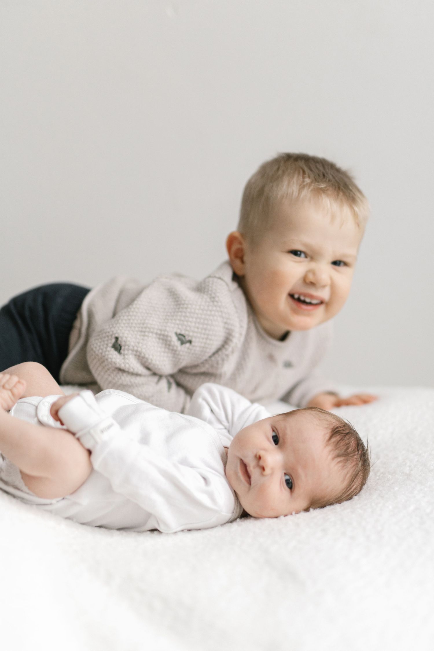 Toddler interacting with newborn sibling on white background.