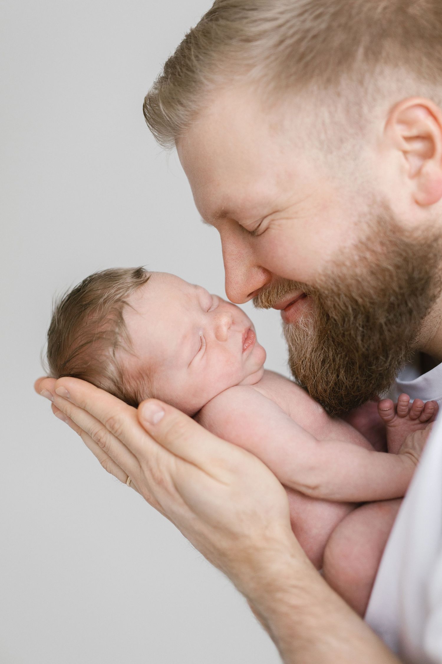Tender moment between a bearded father and newborn baby in soft natural light.