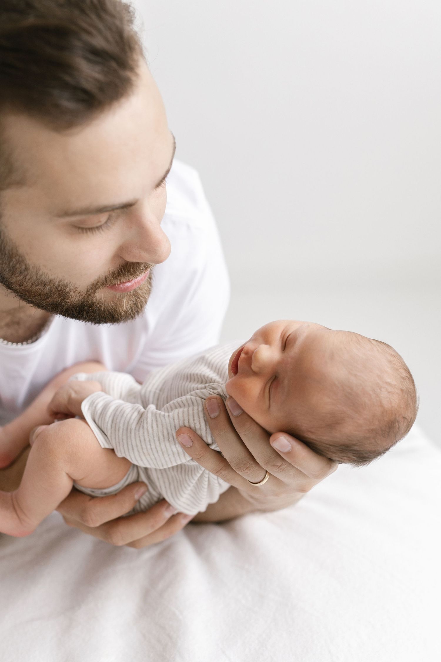Tender moments of parent cradling newborn baby in white setting.