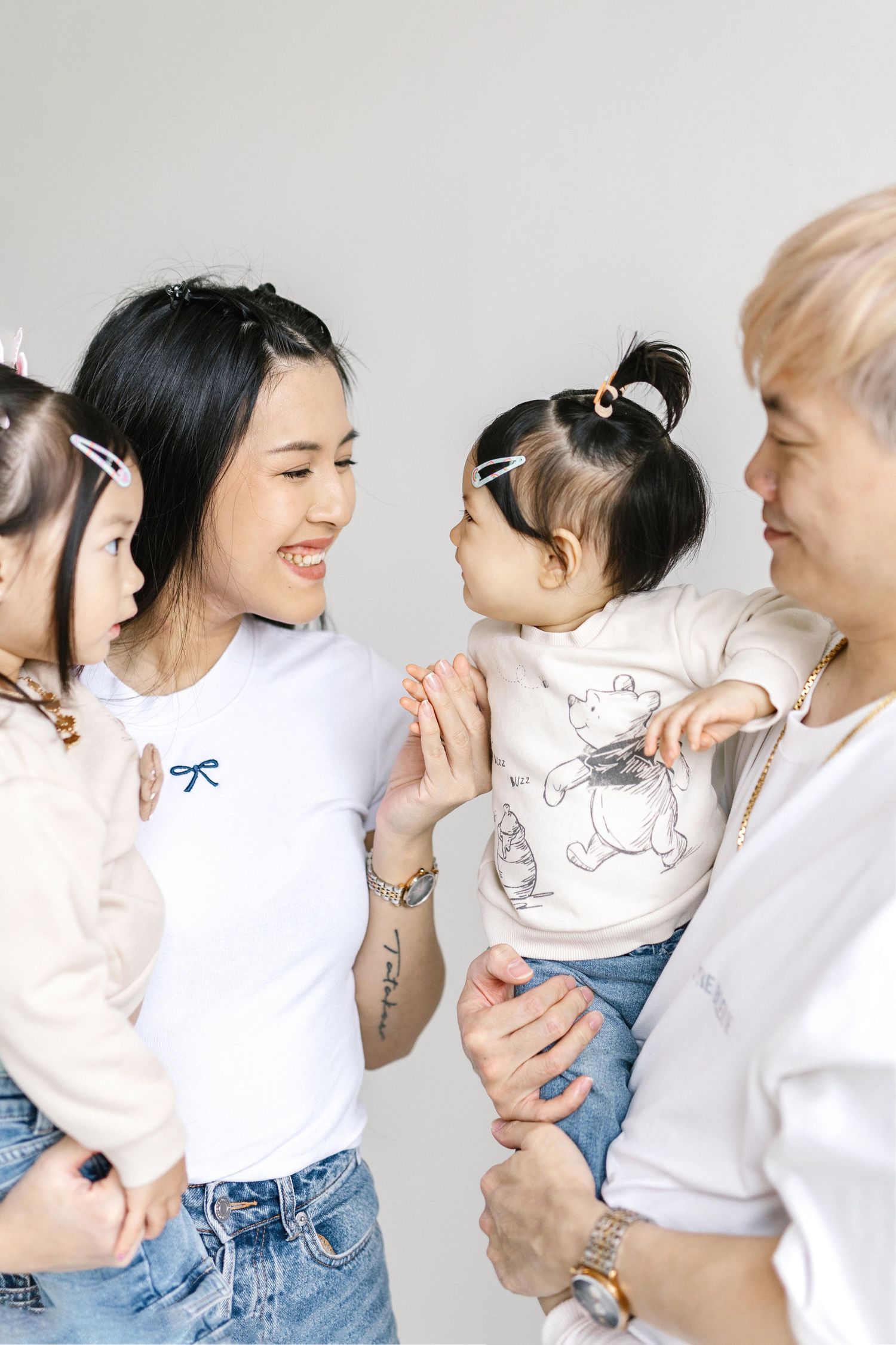Two women holding toddlers facing each other, smiling warmly in a bright studio setting.