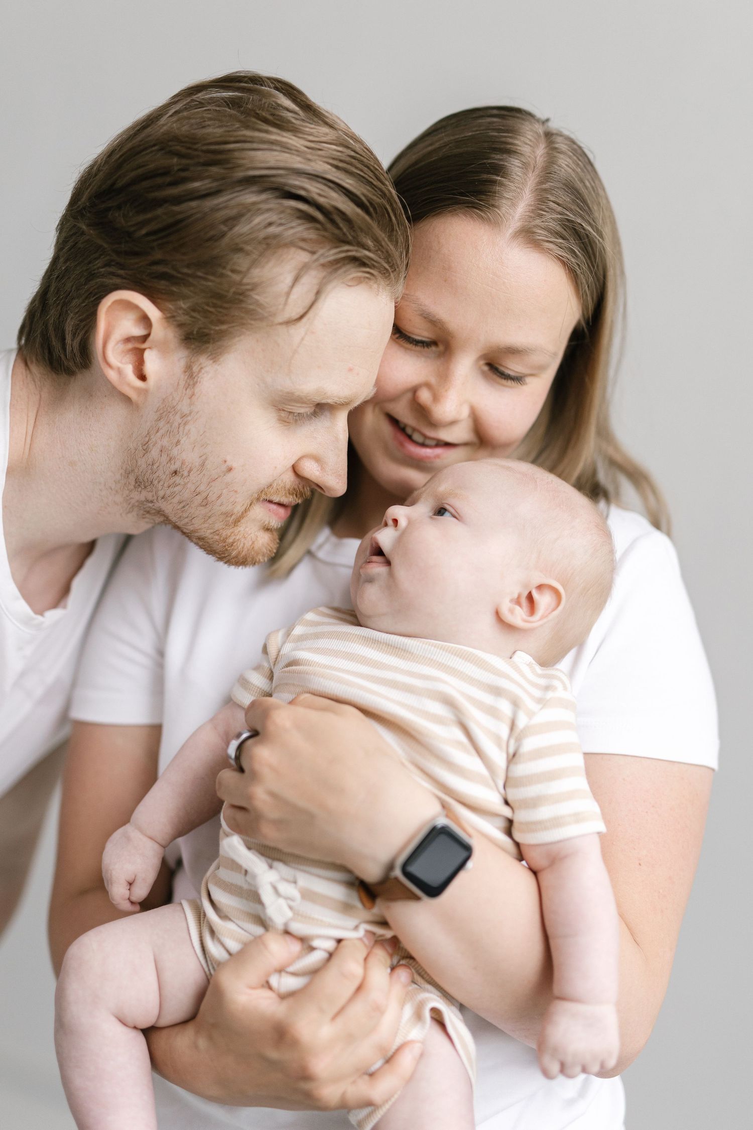 A young couple in white t-shirts tenderly holding their newborn baby, sharing a loving family moment.