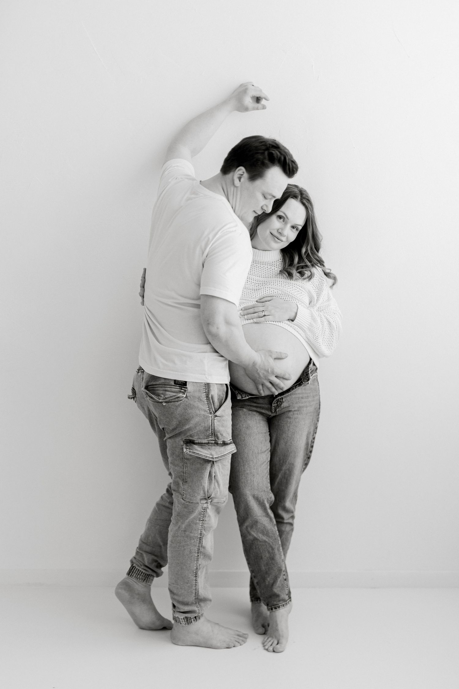 A series of black and white photos showing two people in jeans and white shirts embracing in progressive poses against a wall.