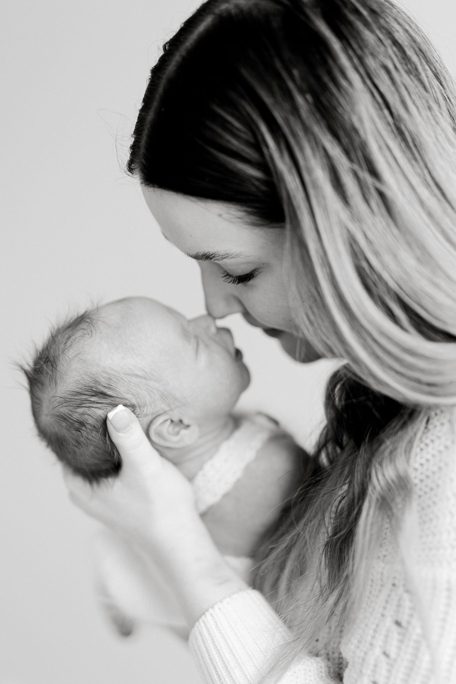 A tender black and white portrait of a mother holding and nuzzling her newborn baby in an intimate moment.