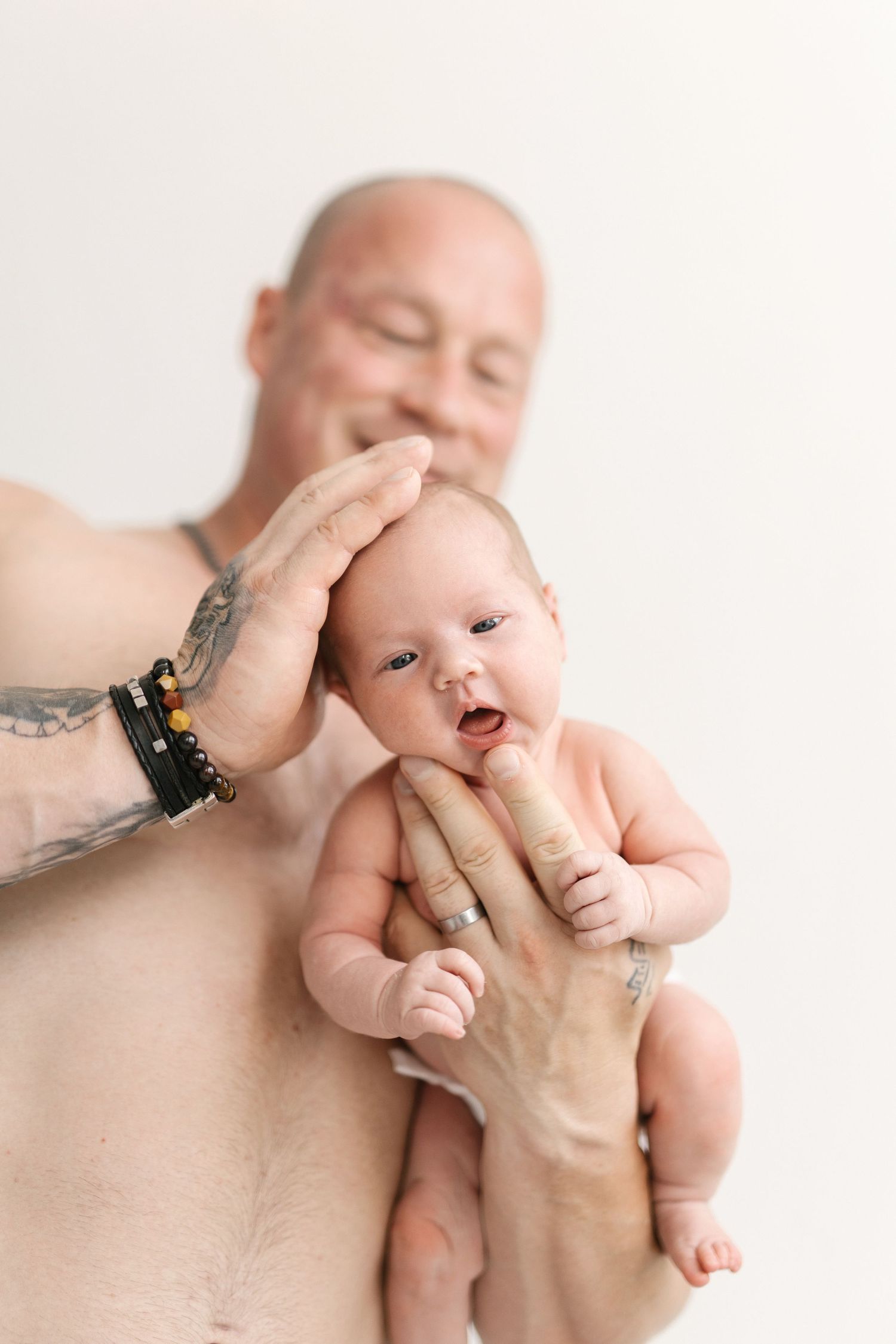 Parent with tattoos holding newborn baby against white background.