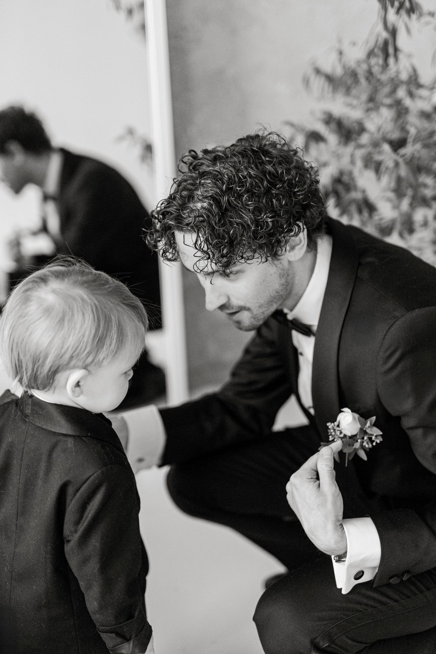Intimate black and white moment between groom and young child during wedding preparations.