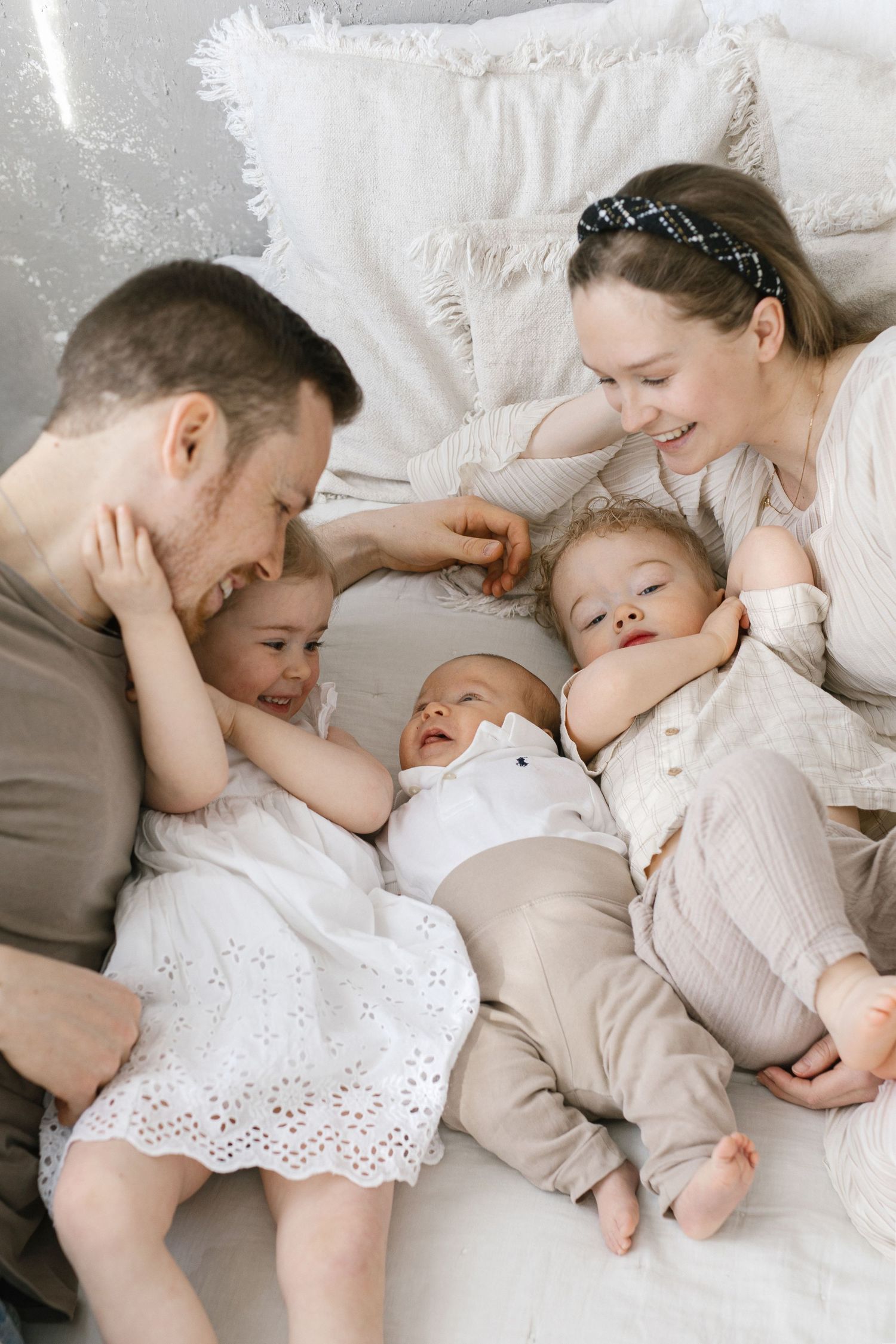 Happy family with two parents and three young children laughing and cuddling together on a cozy white bed.