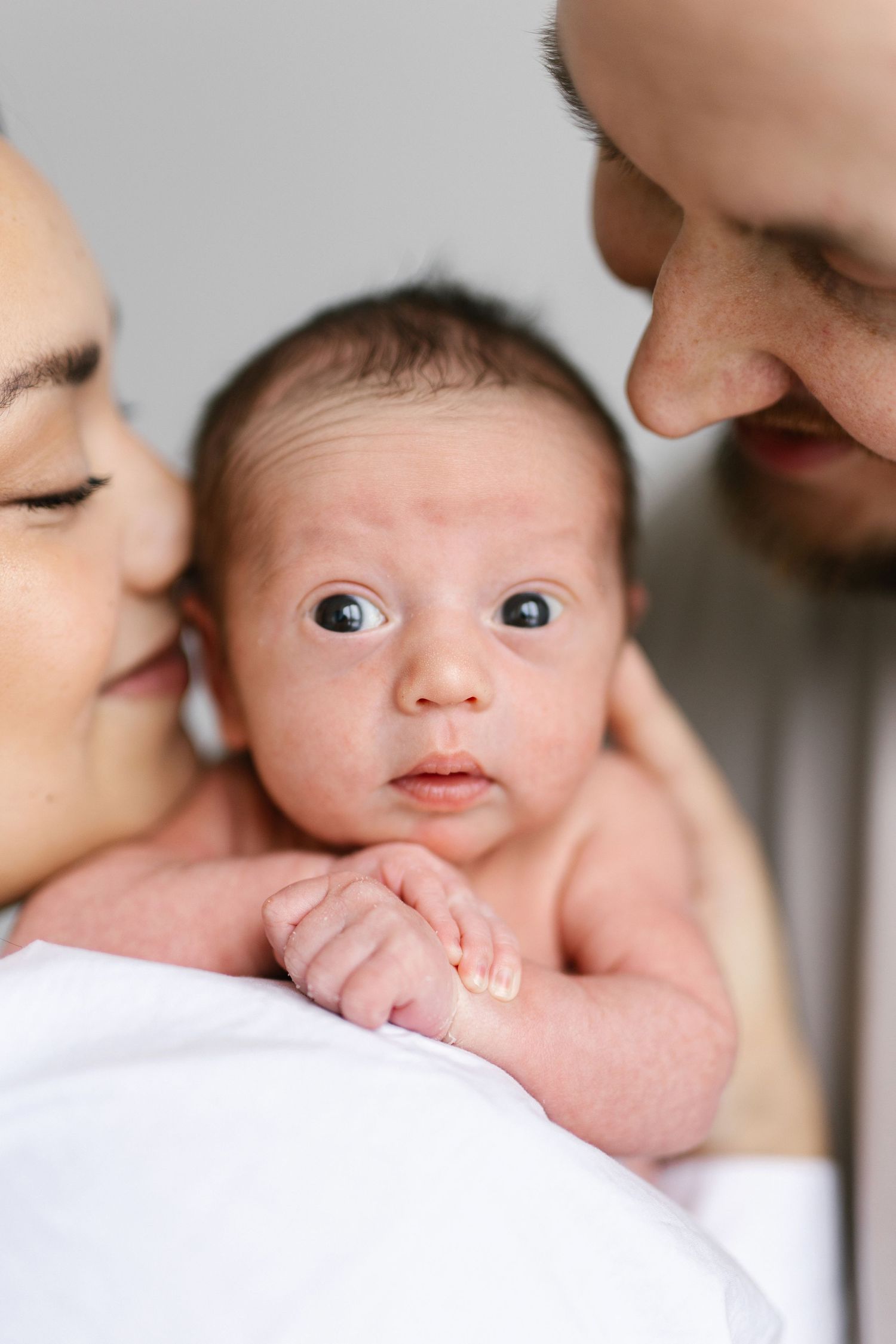 Tender moment between parents and newborn baby against light background.