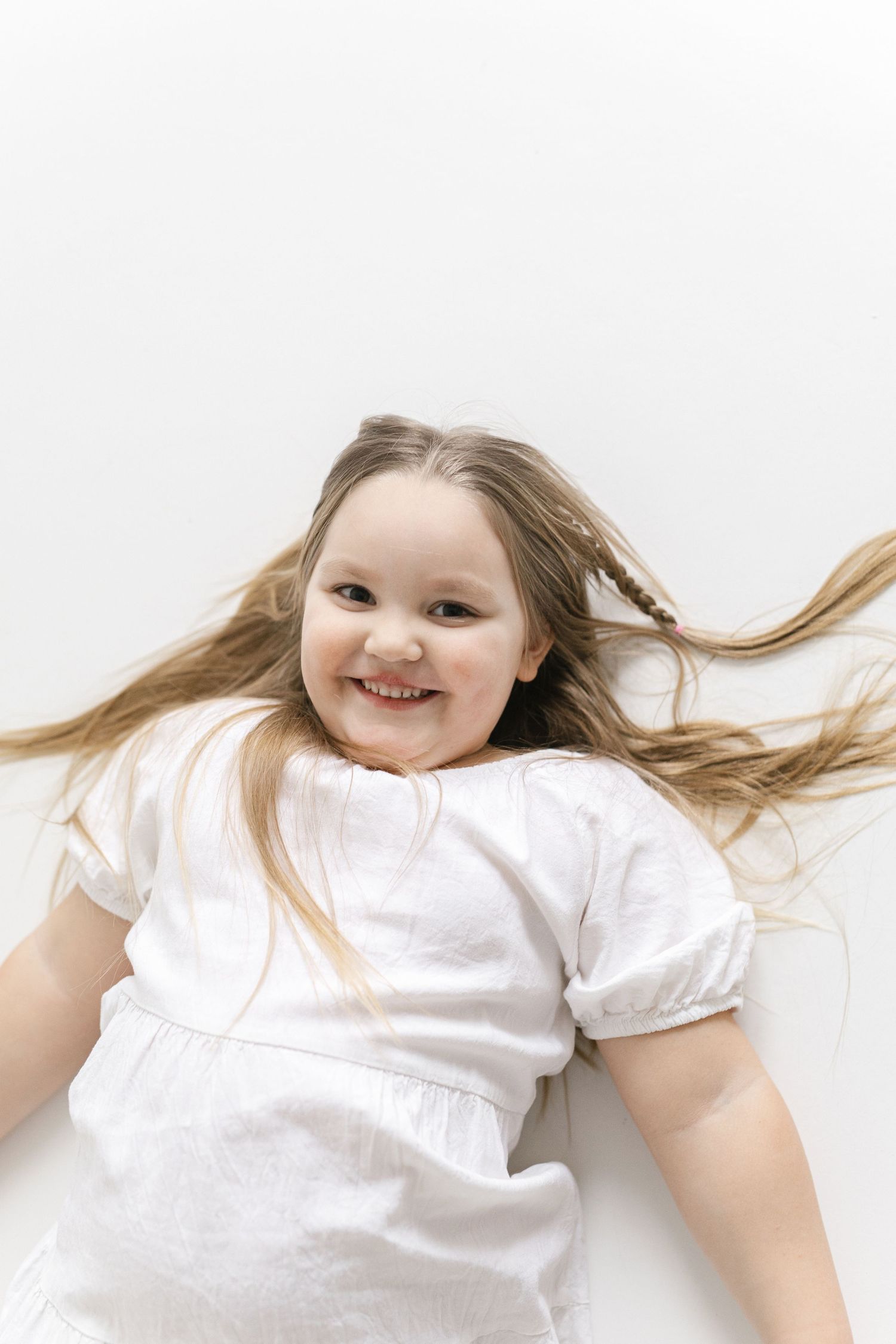 Lying on white background wearing white dress with hair spread out in playful poses.